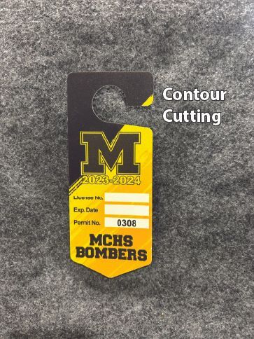 Yellow and black MCHS Bombers door hanger with large M logo, hole at top, on gray surface