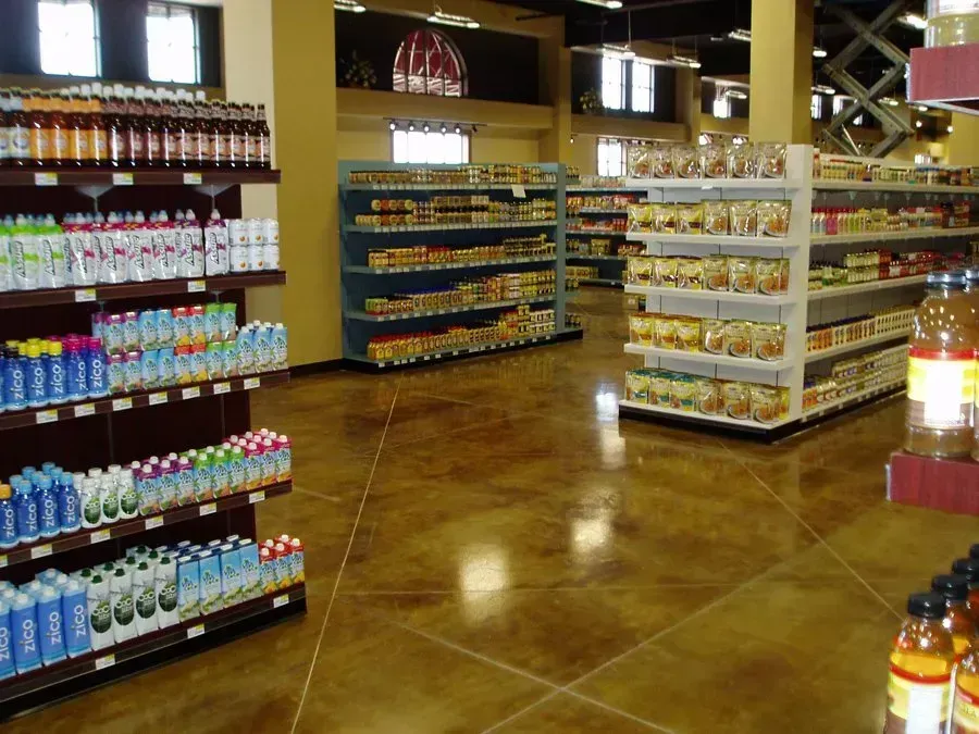 Grocery store interior with aisles of shelves stocked with various packaged food and beverages. Brown floor.