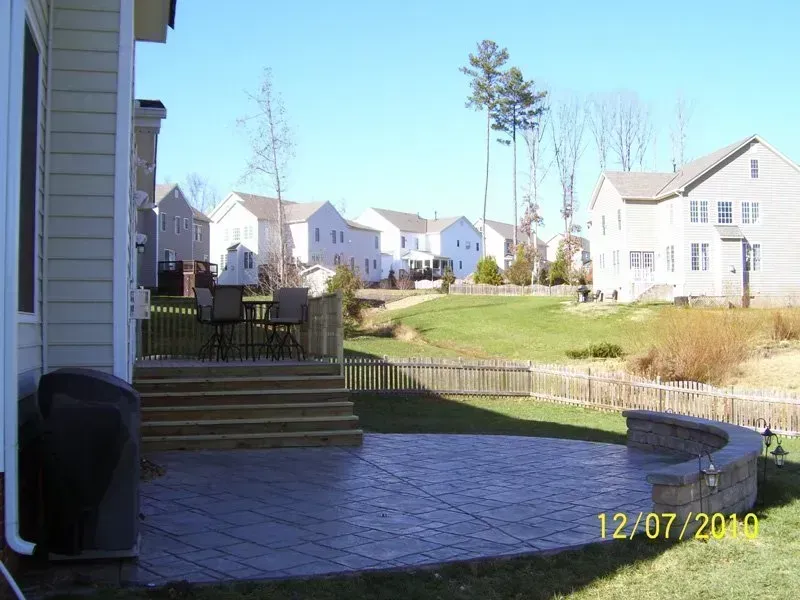 Backyard patio with steps, outdoor furniture, curved retaining wall, and green lawn on a sunny day.