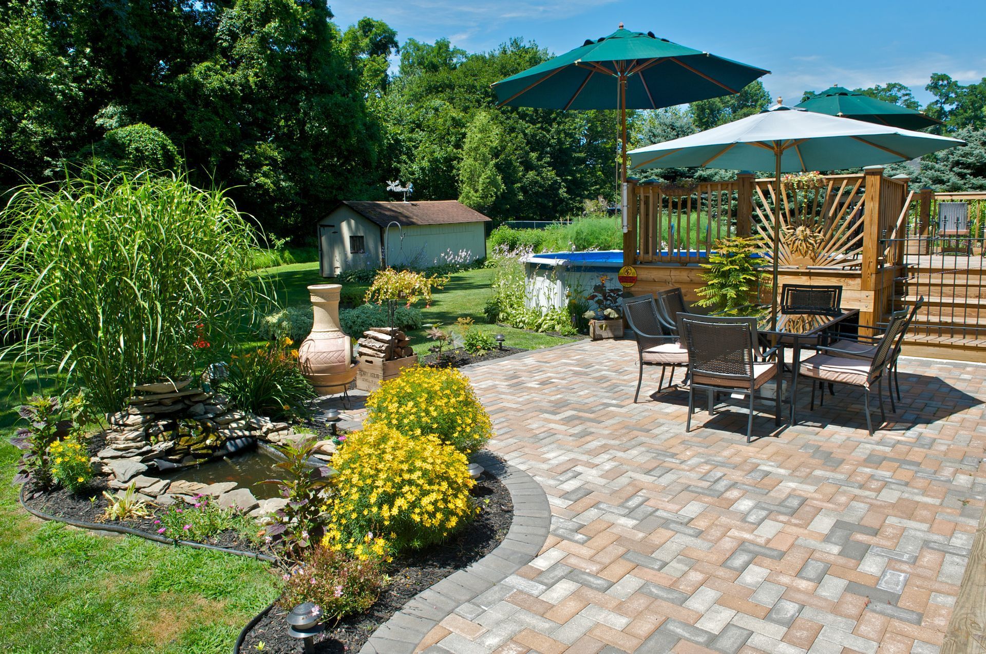 Patio with brick pavers, table, chairs, umbrellas, small pond, and lush greenery.