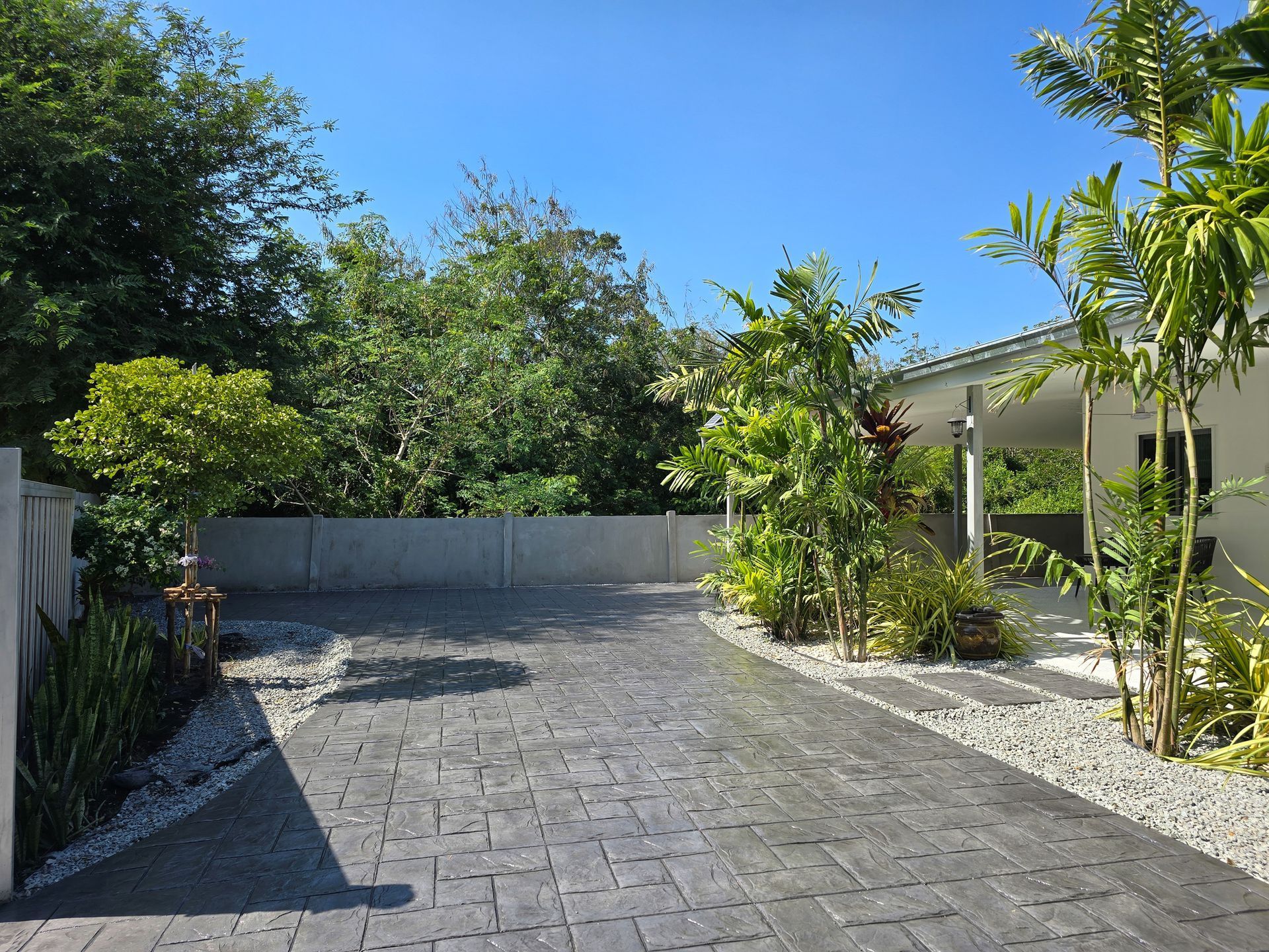 Driveway leading to a white house with landscaping, concrete pavers, and blue sky.