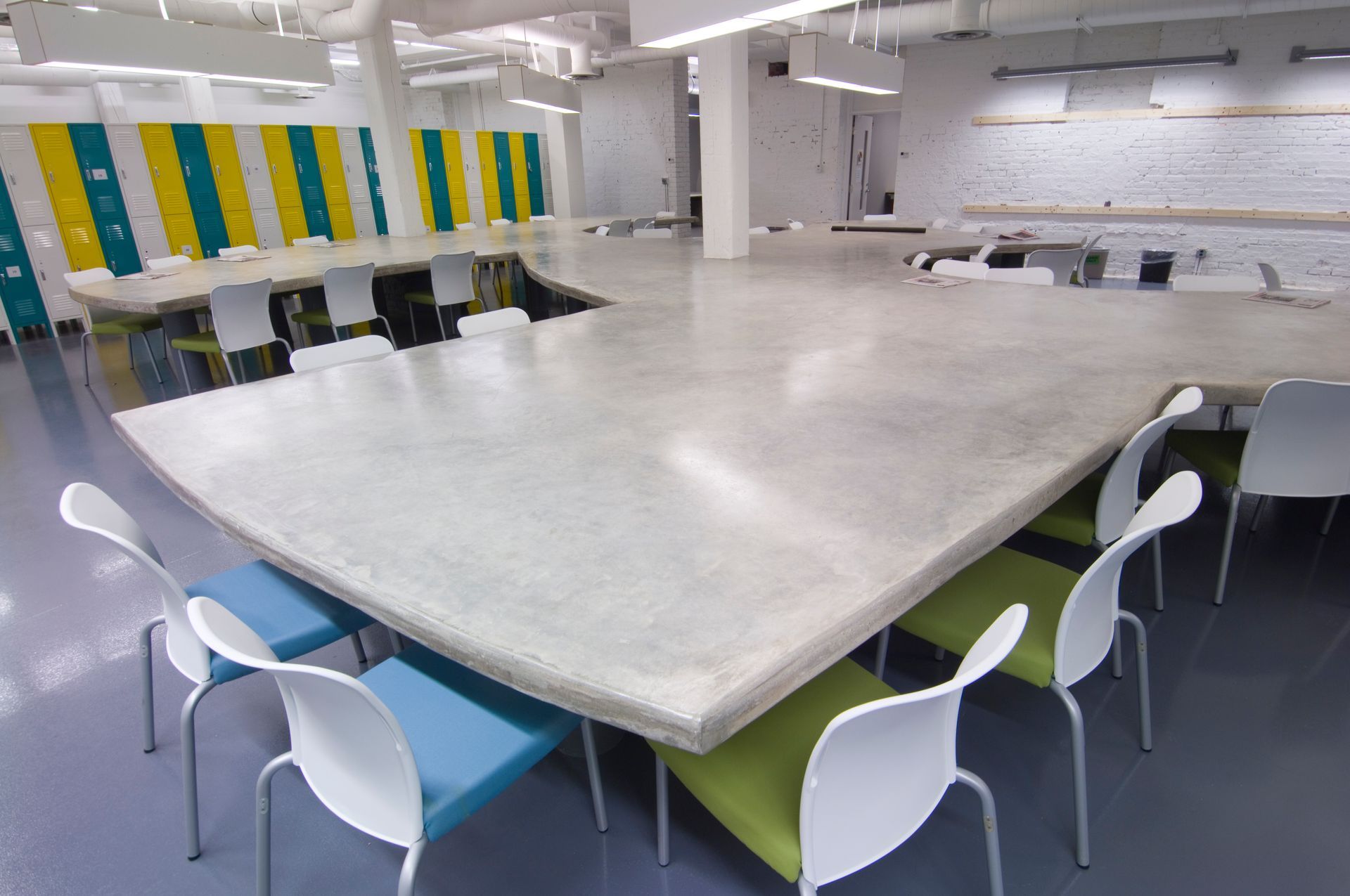 Large, light-colored table with curved edges, surrounded by white and colored chairs in a modern, open room.