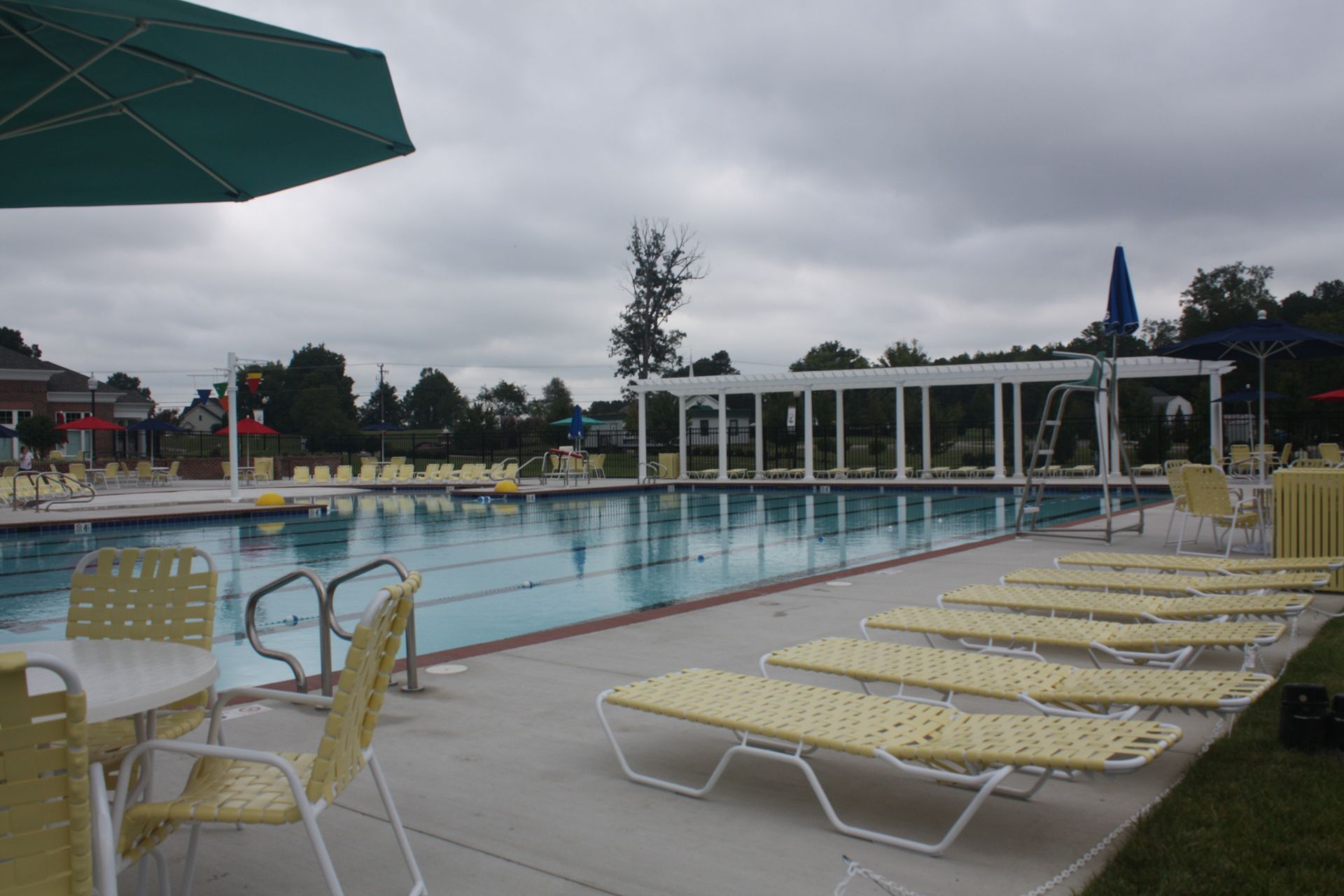 Pool with lane lines, lounge chairs, and an umbrella under cloudy skies.