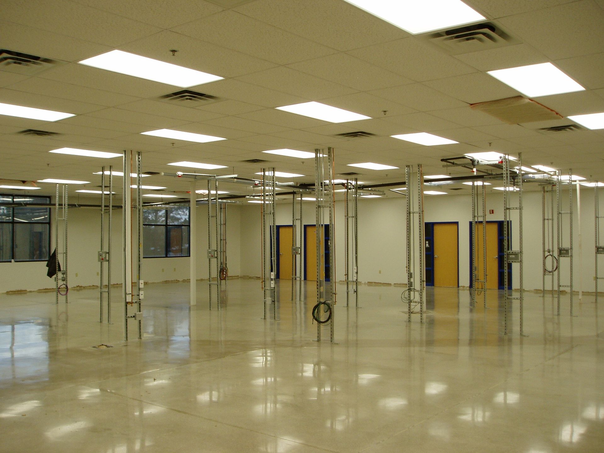 Empty room with metal support structures, bright overhead lights, doors, and glossy floor.