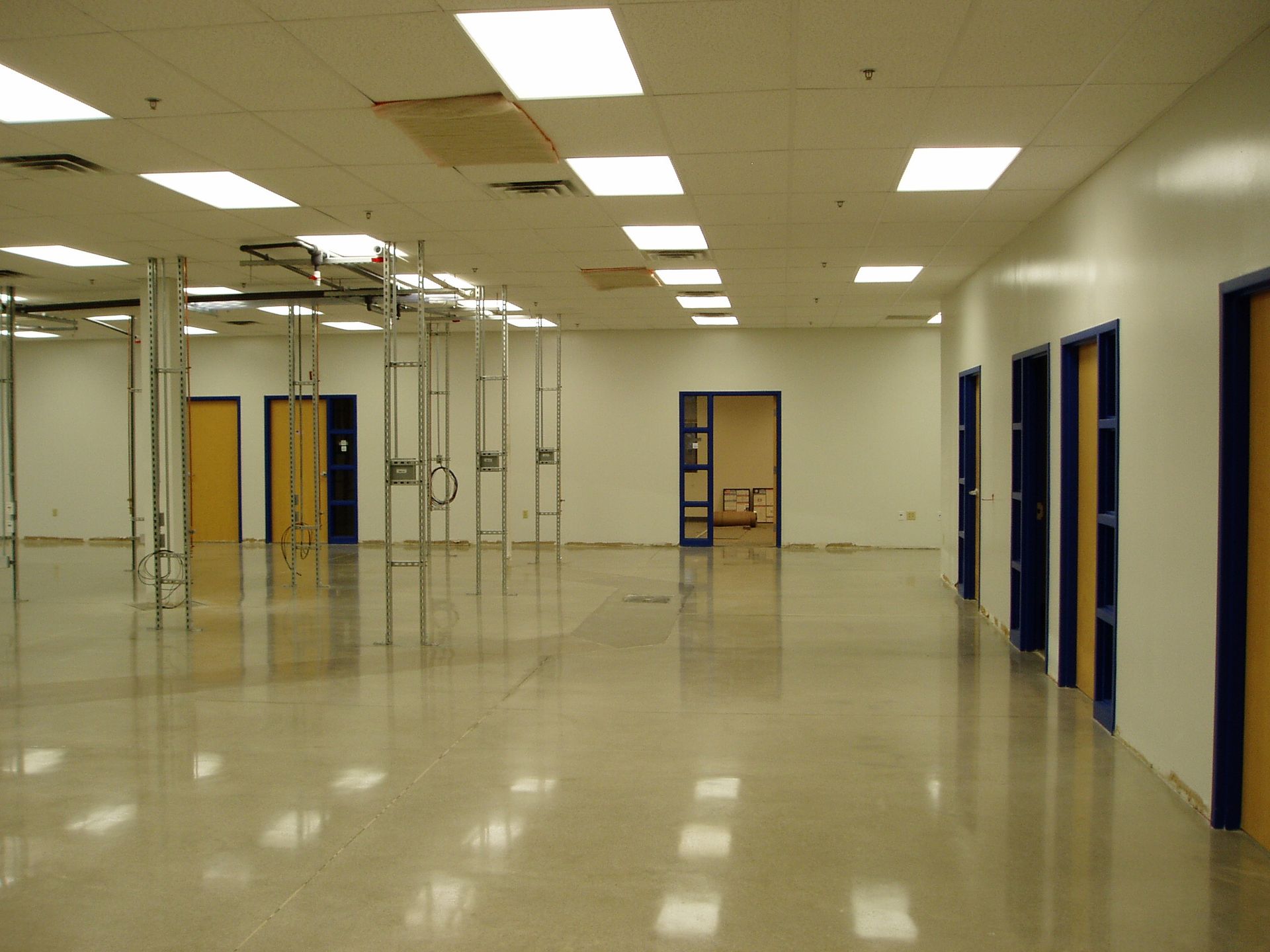 Large empty room with shiny floor, bright ceiling lights, and several closed doors along the right wall.