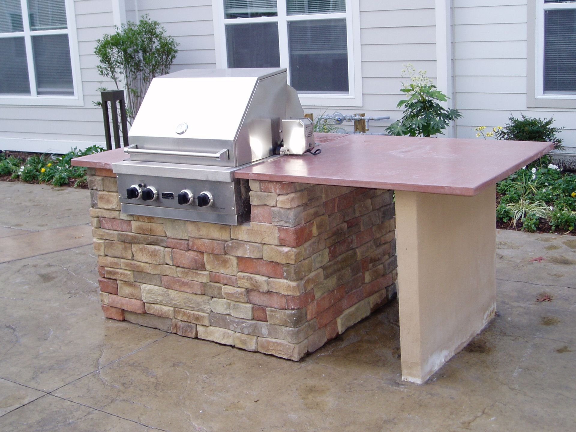 Outdoor grill built into a brick and concrete island with a countertop.