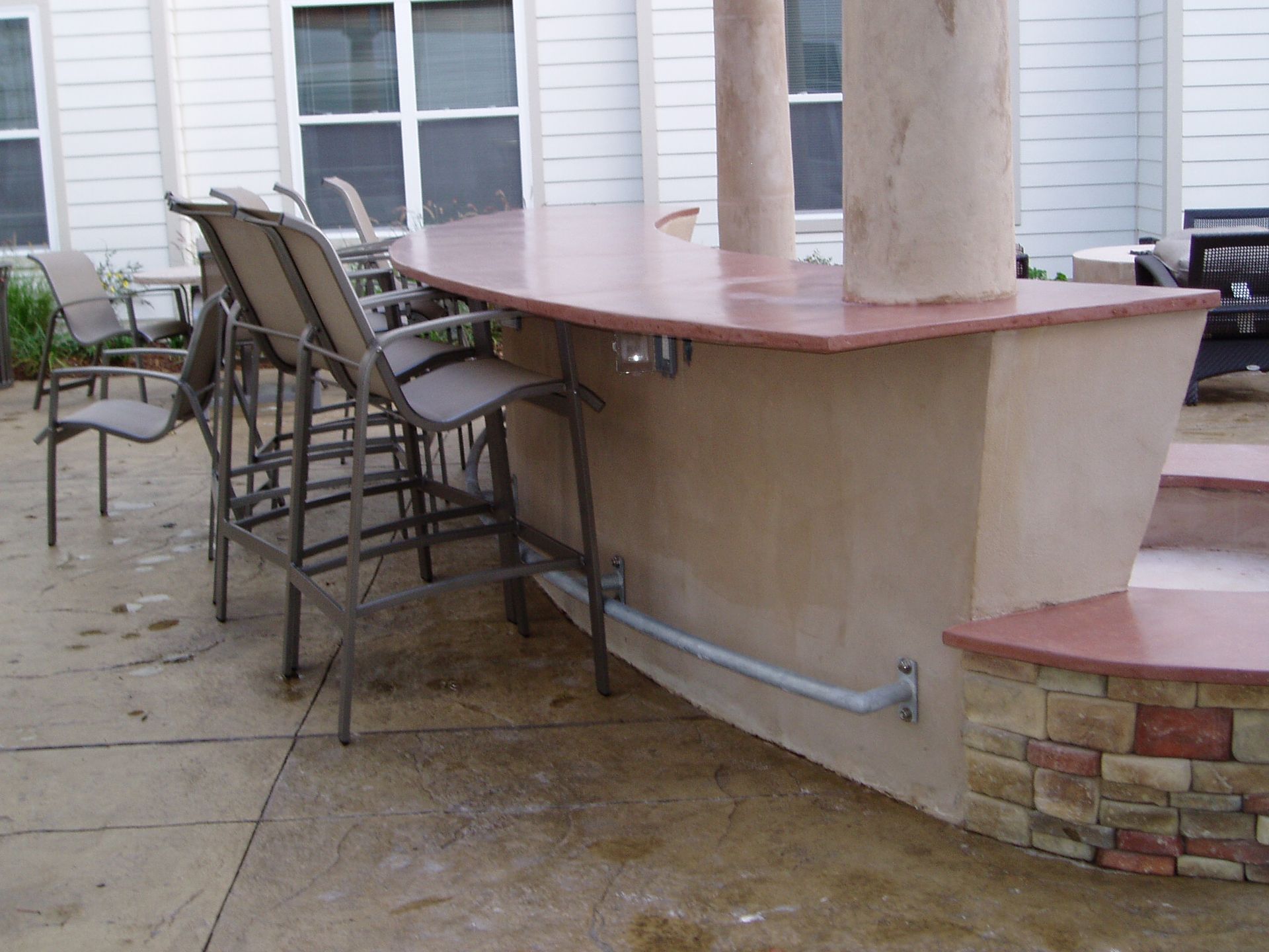 Outdoor bar with stools, red countertop, and stone detailing, set in a backyard.