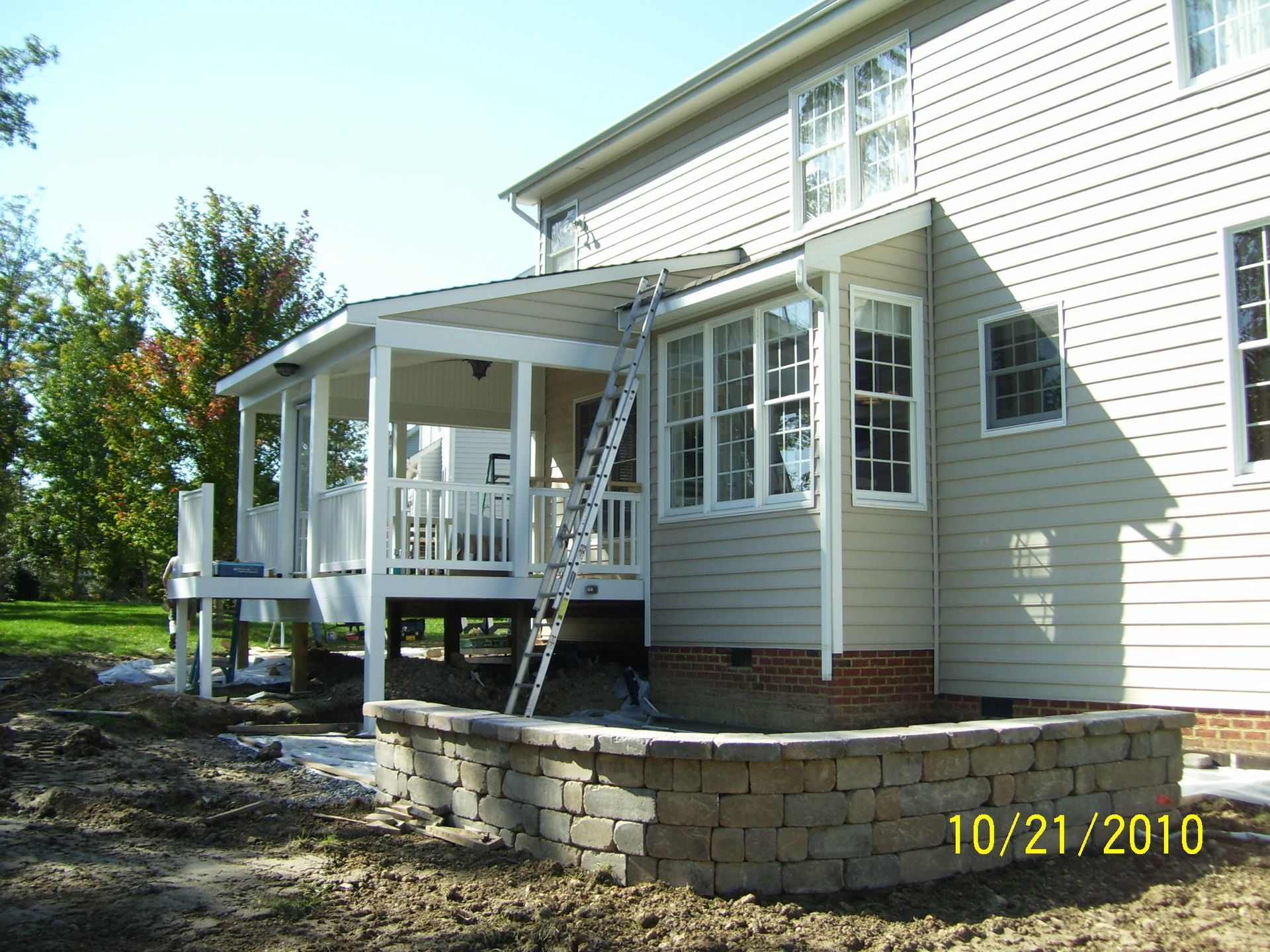 Deck addition to a house with a retaining wall. Ladder leans against the house, construction is ongoing.