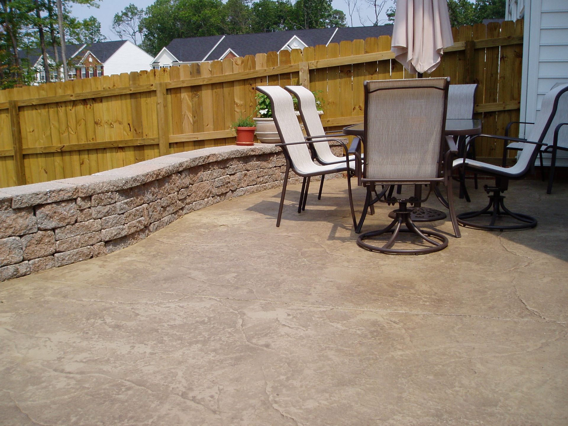 Patio with concrete floor, stone retaining wall, wooden fence, and patio furniture.