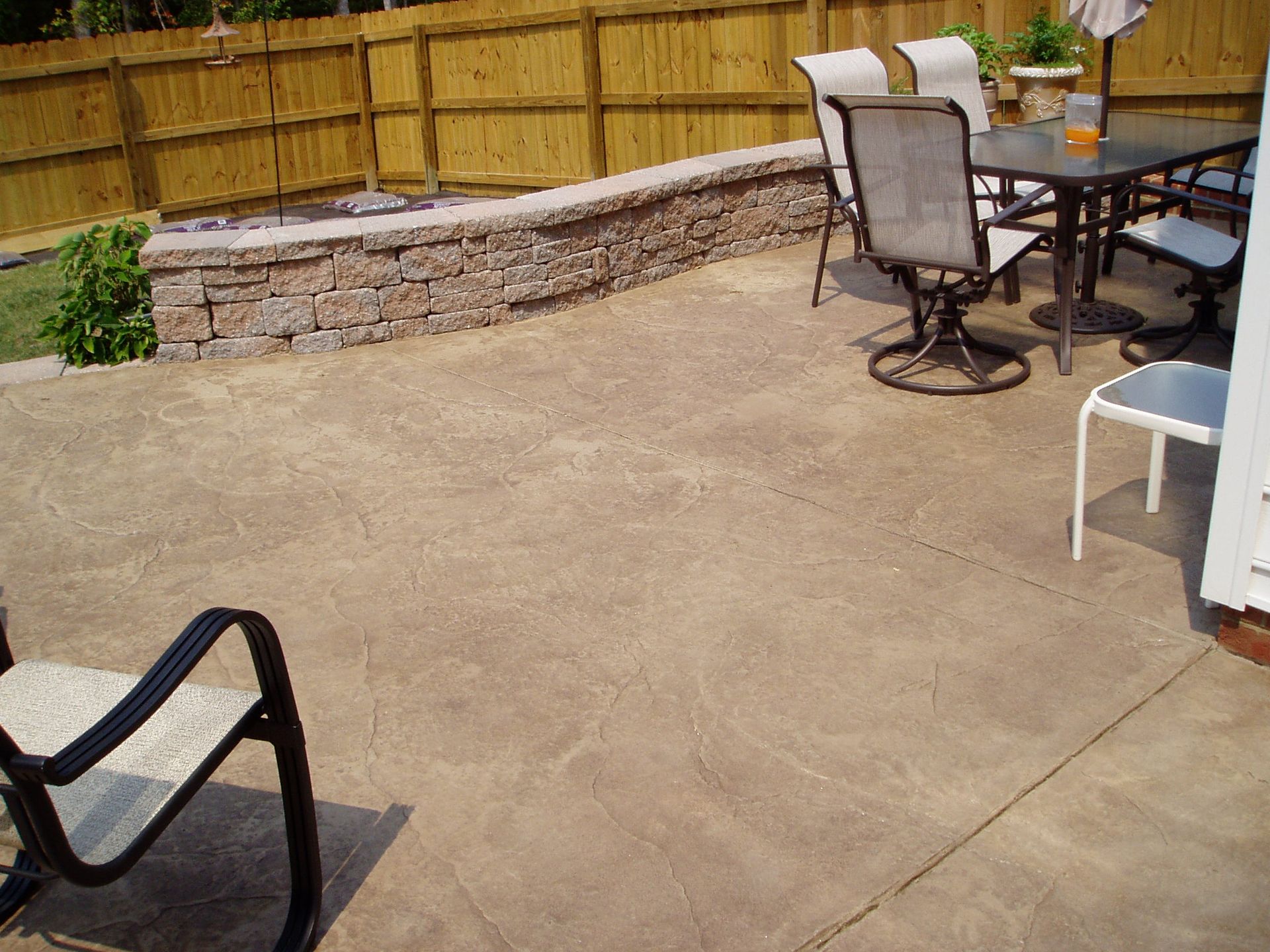 Concrete patio with dining table, chairs, and a retaining wall.
