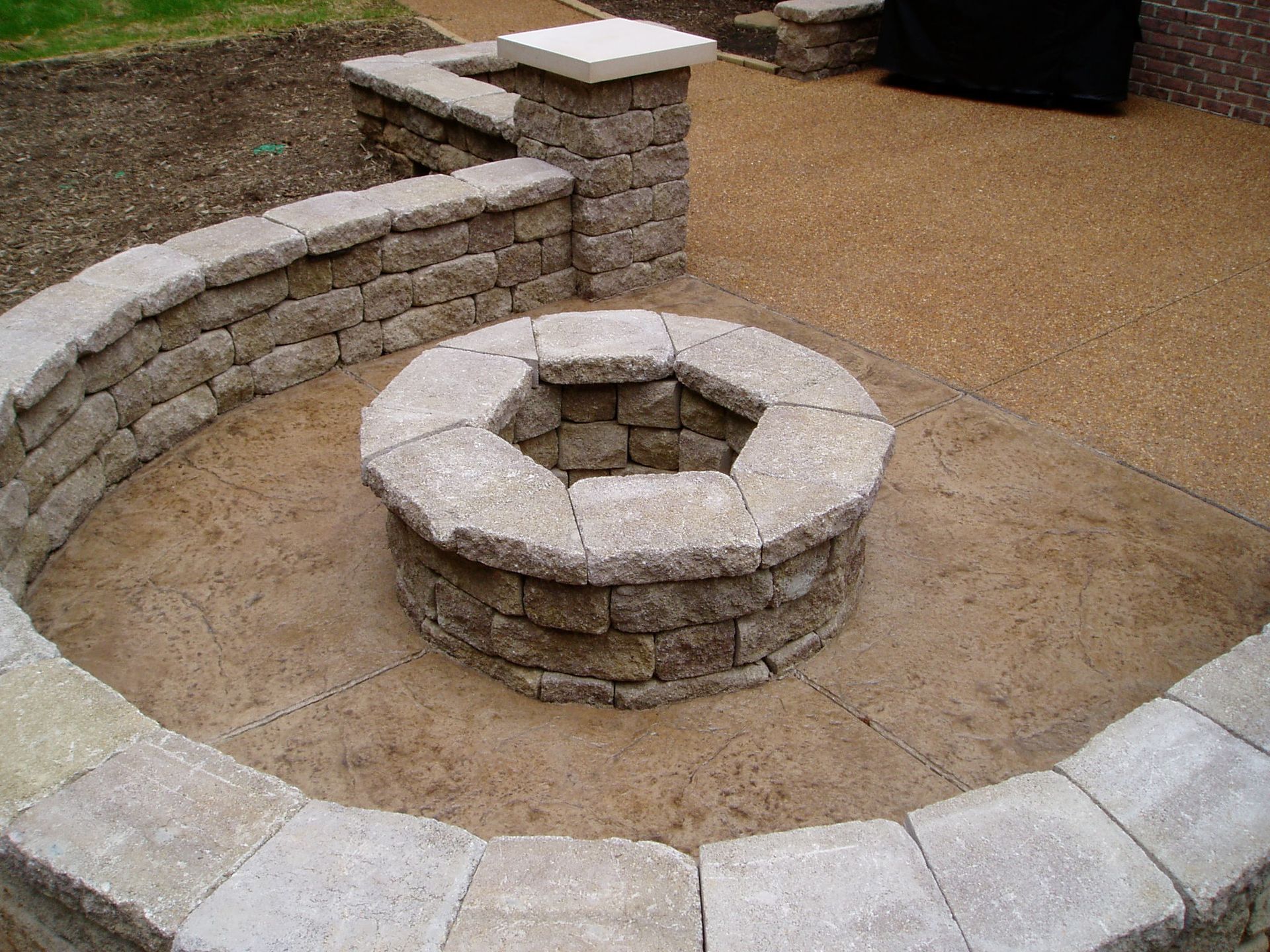 Stone fire pit surrounded by low walls on a gravel patio.