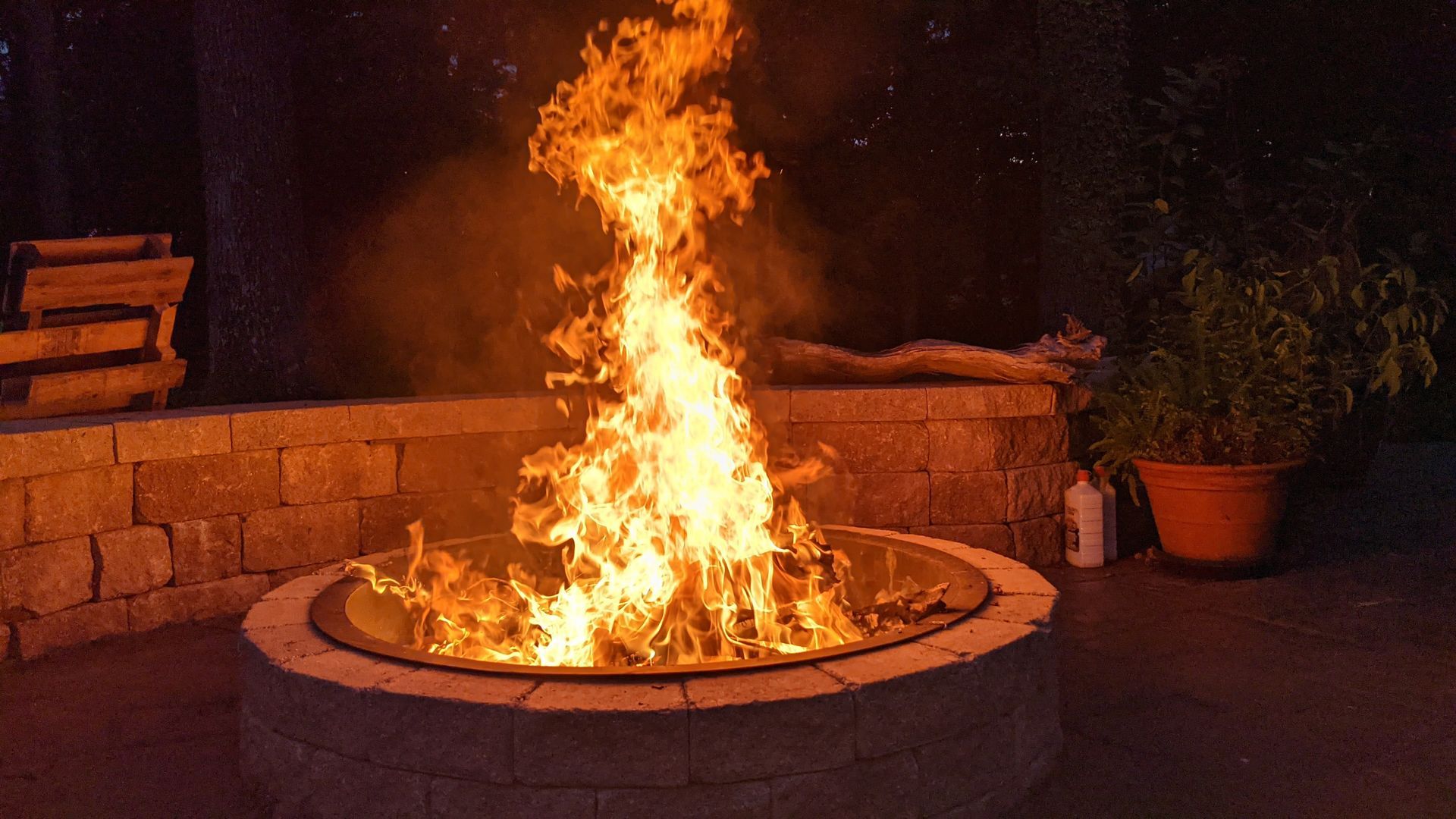 Bright flames burning in a stone fire pit, illuminating a dark patio setting.