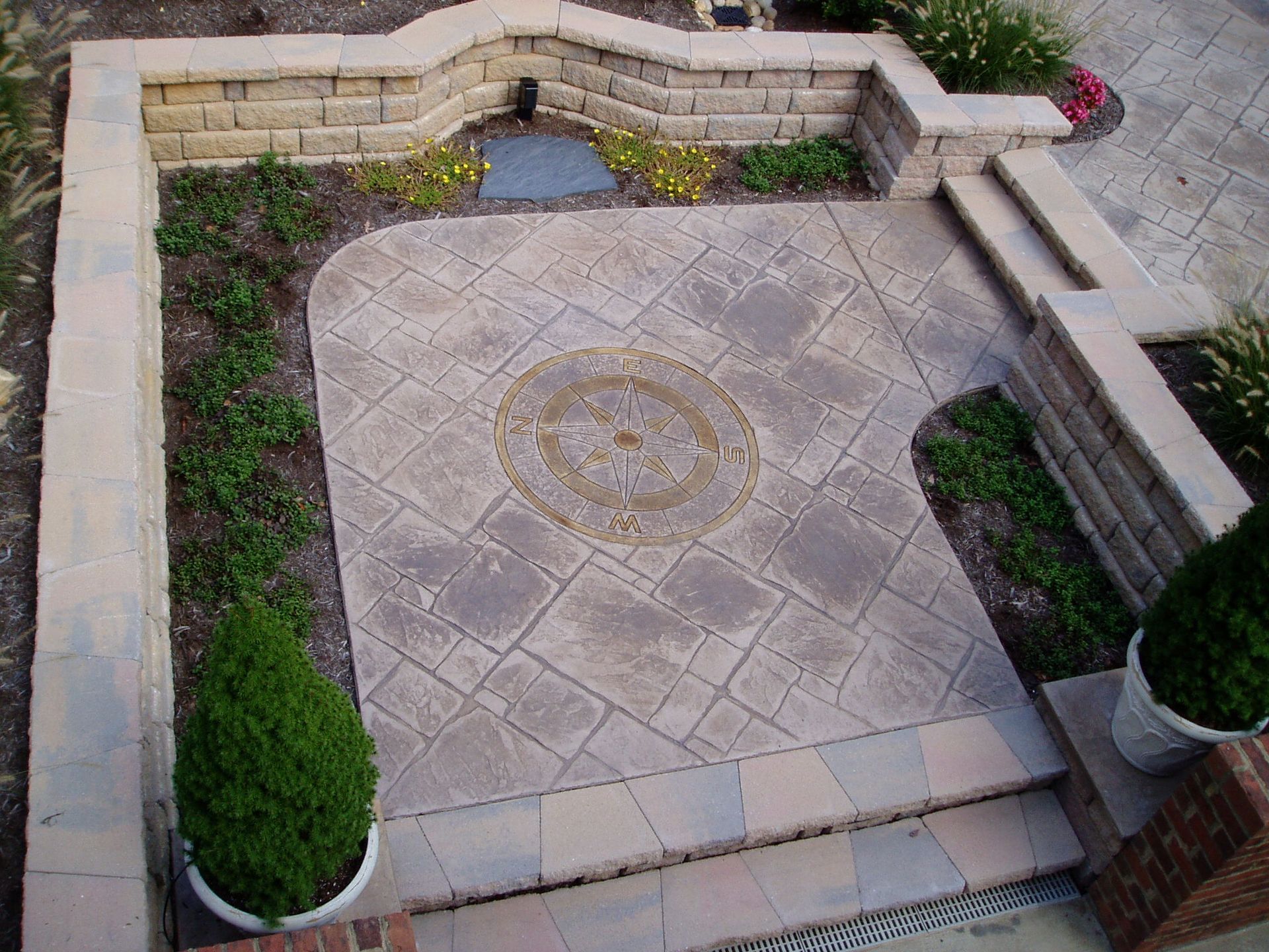 Stone patio with built-in planter boxes and decorative central circle design, surrounded by greenery.