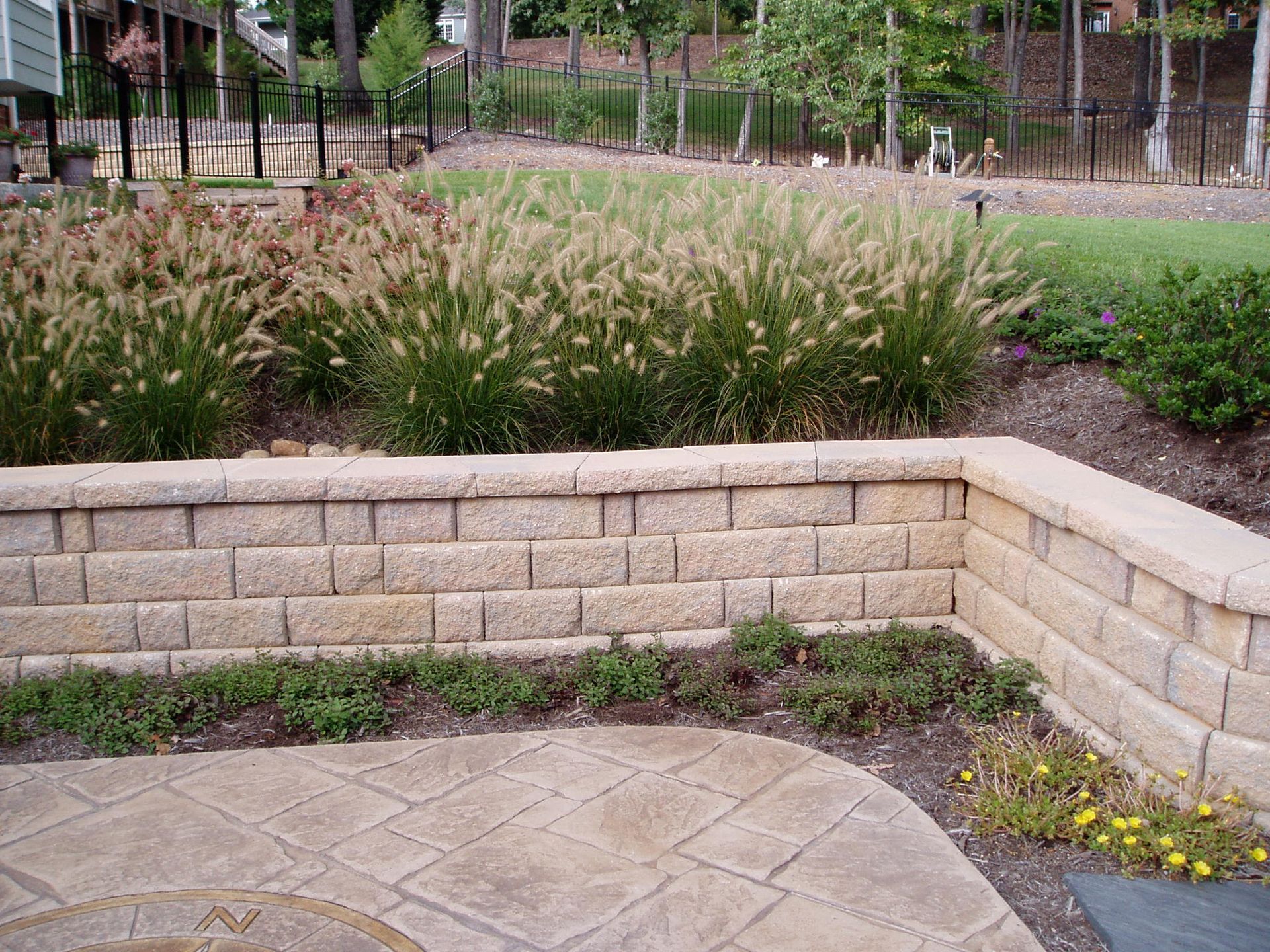 Stone retaining wall with ornamental grasses and a paved patio.