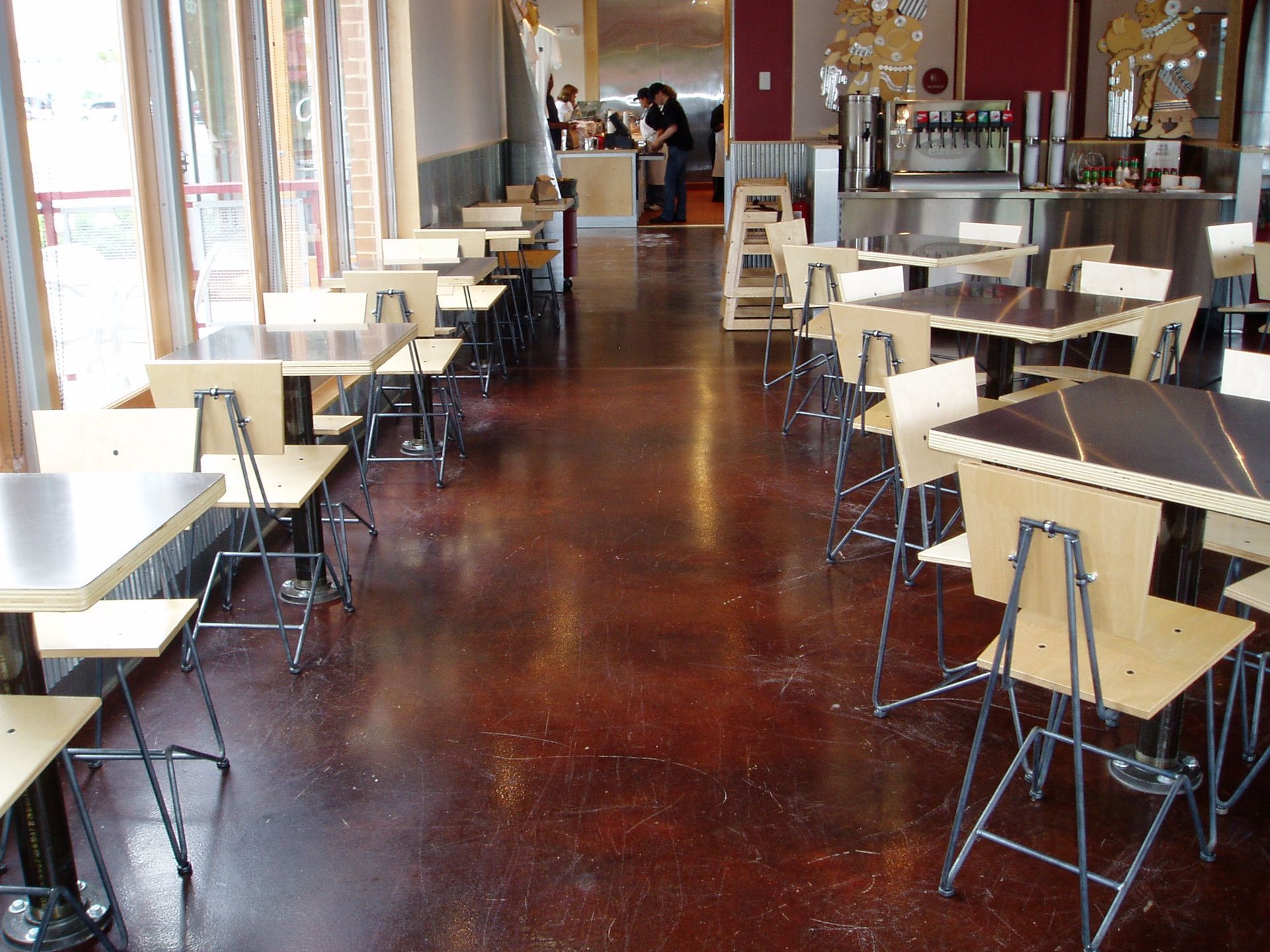Empty restaurant interior with brown floor, tables, chairs, and a drink station.