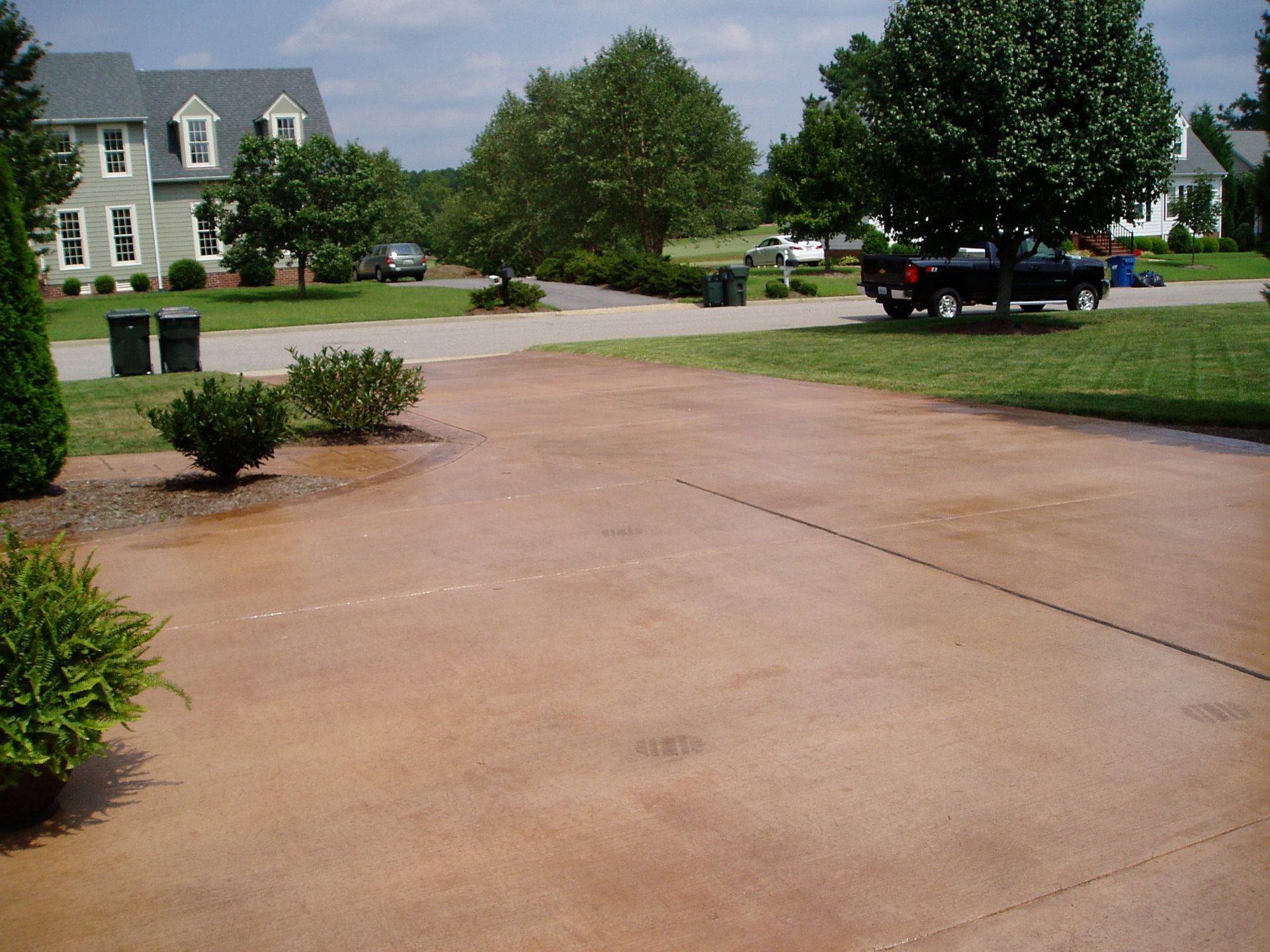 Brown stained concrete driveway in a suburban setting, with grass and houses.