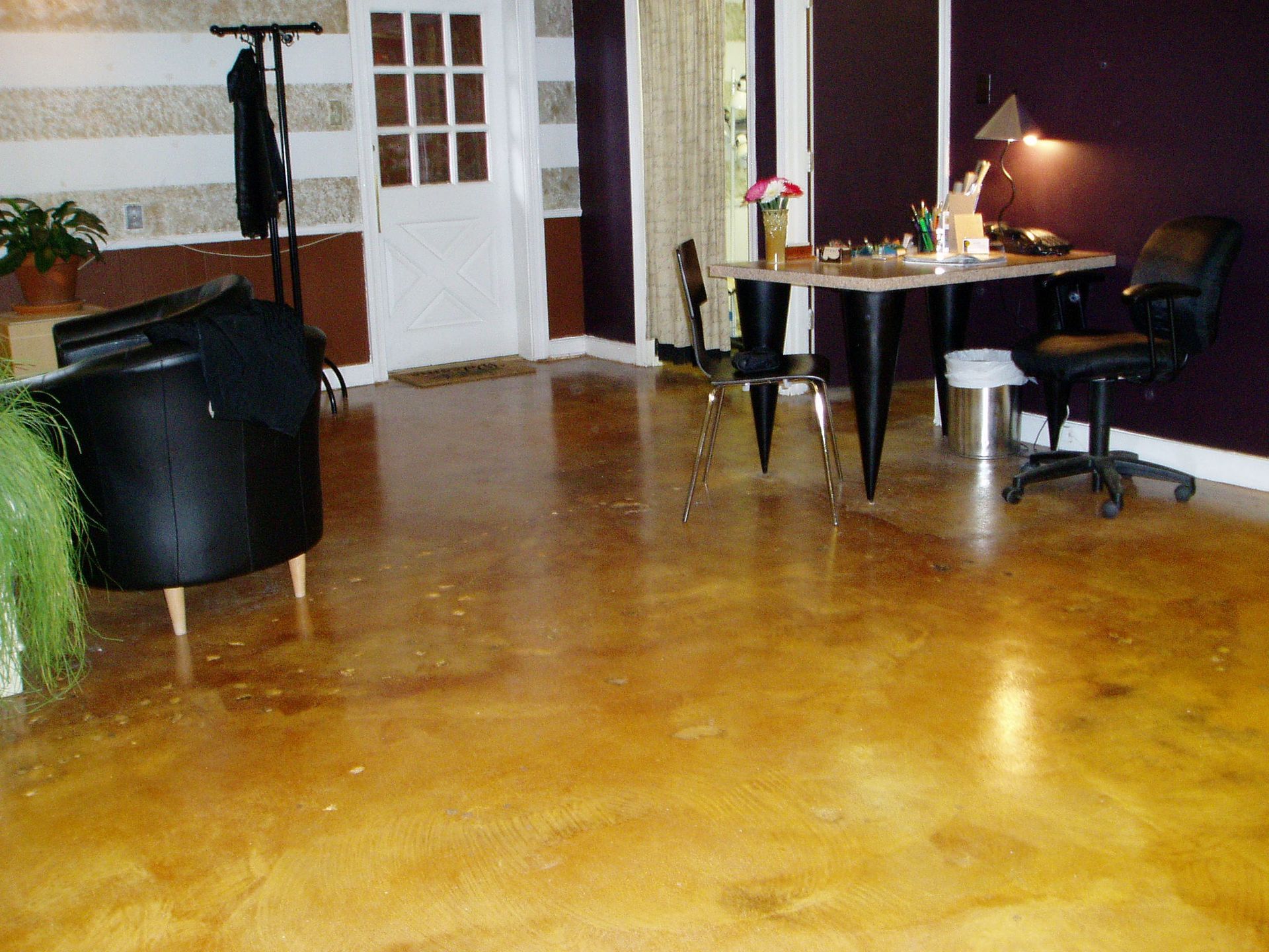 Room with yellow-brown stained concrete floor, desk, chairs, and white door.