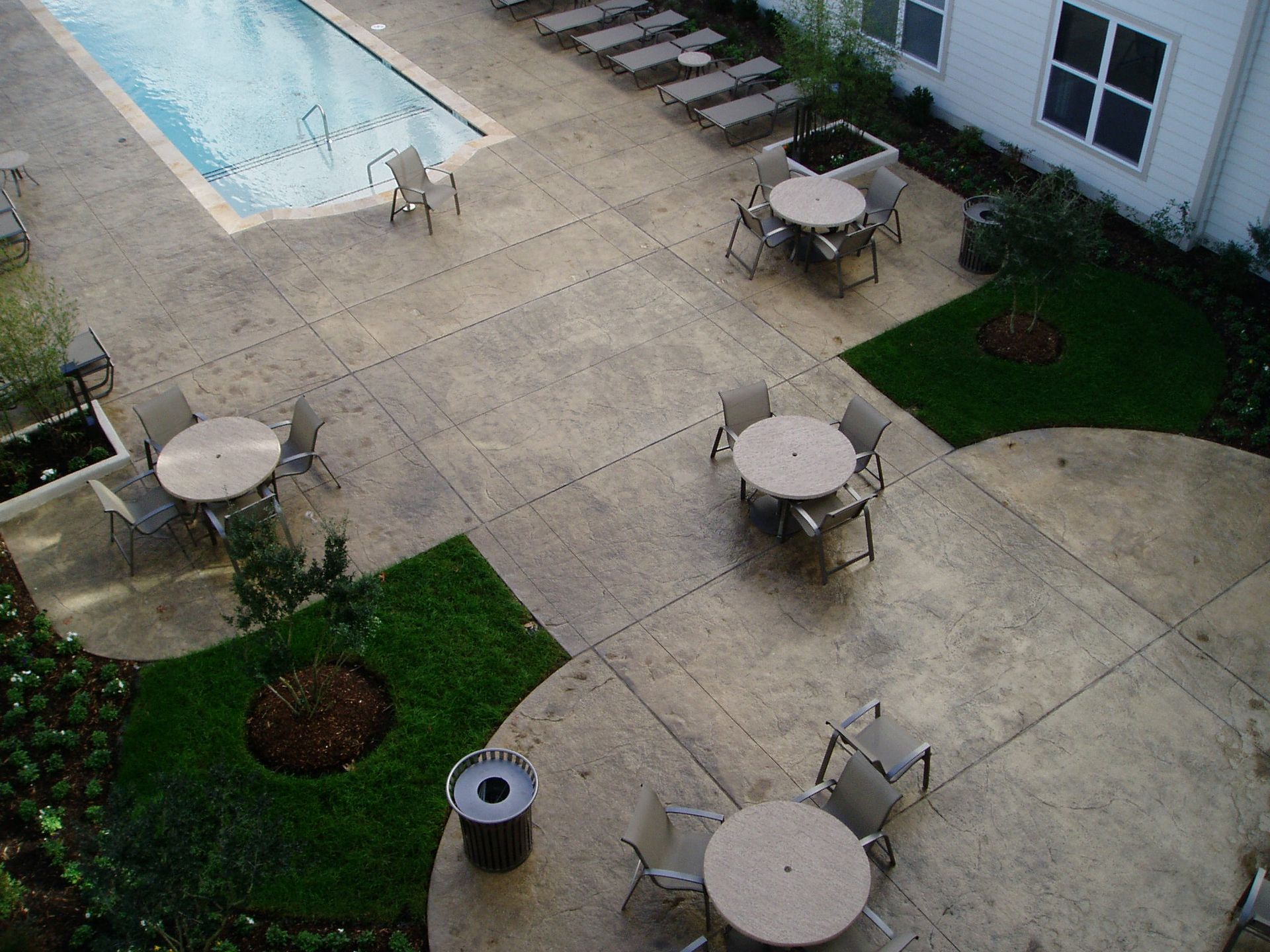 Courtyard with pool, tables, chairs, and landscaping. Concrete patio with neutral tones and outdoor seating.