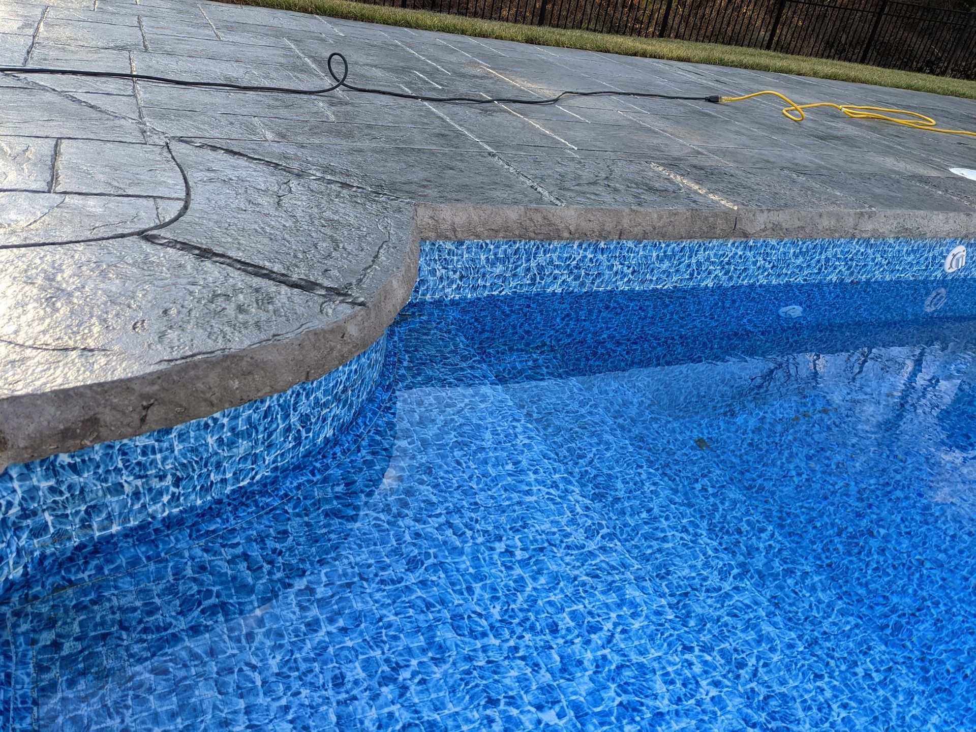 Blue pool with mosaic tile edge, gray stamped concrete patio.