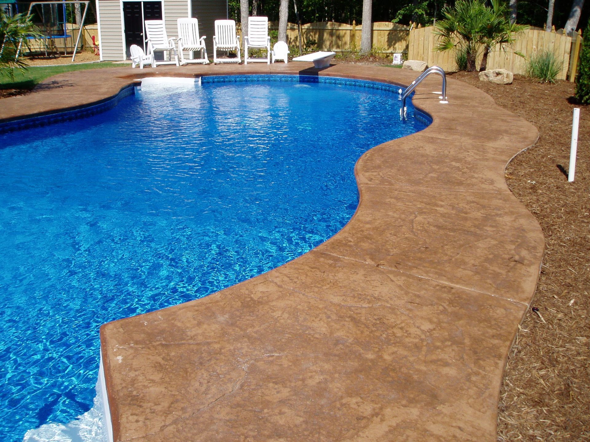Brown stamped concrete pool deck surrounds a blue swimming pool.