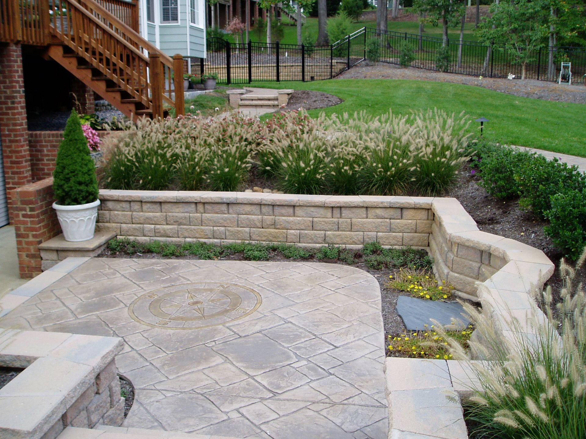 Brick patio with retaining wall, landscaping, and steps leading to a wooden deck.