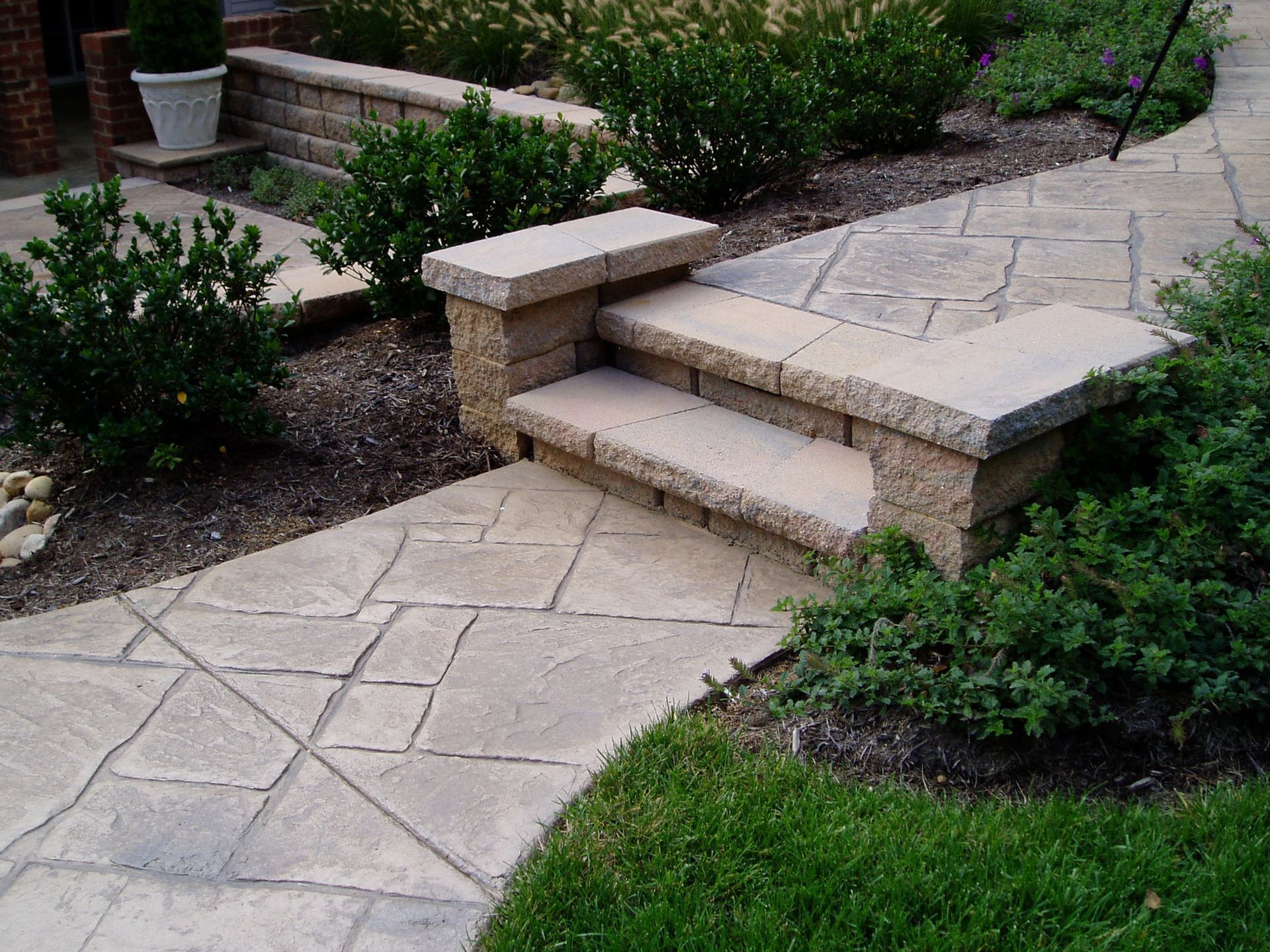 Stone walkway with steps, landscaping, and bushes.