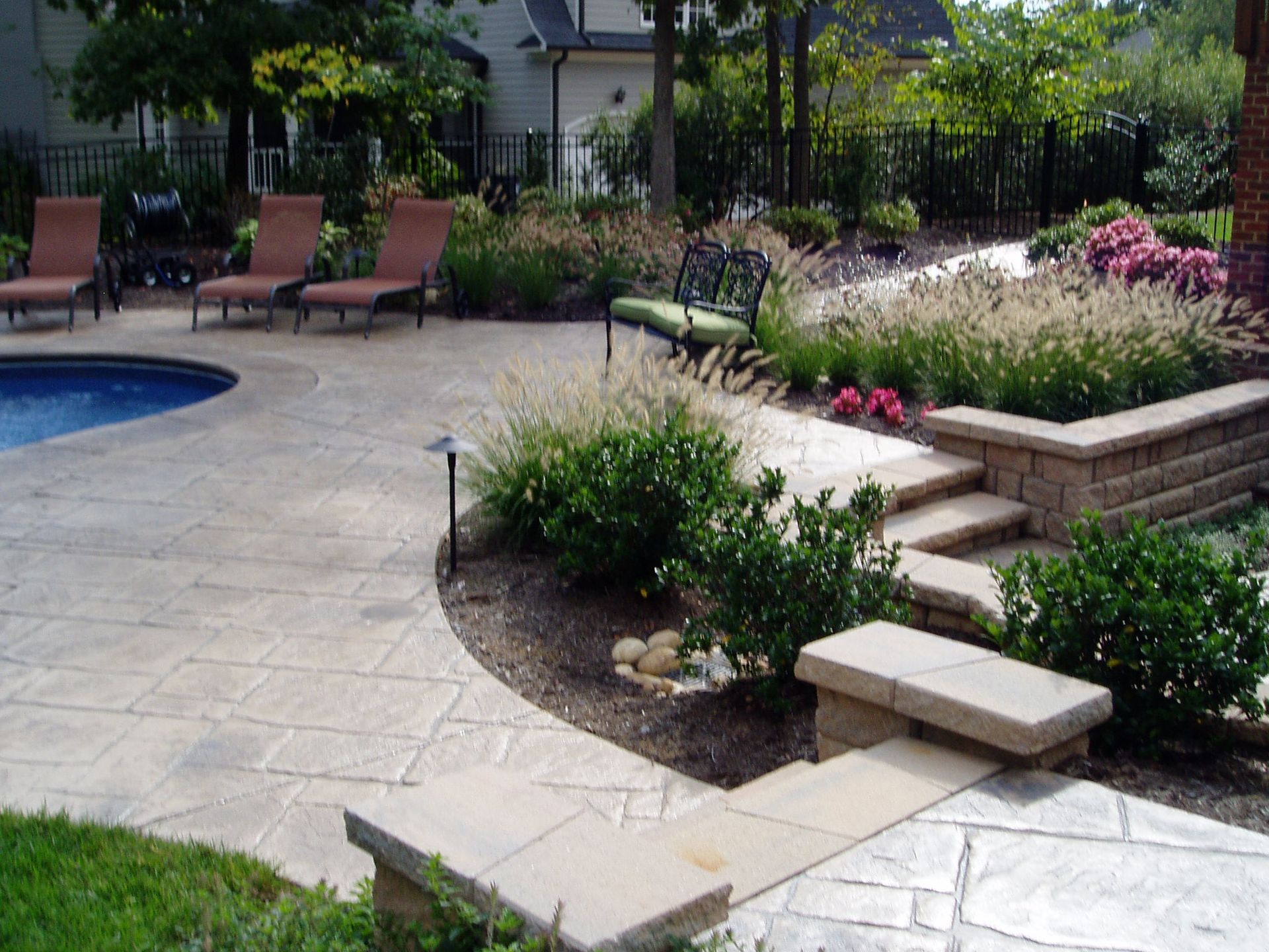 Stone patio with pool, landscaping, lounge chairs, and steps.