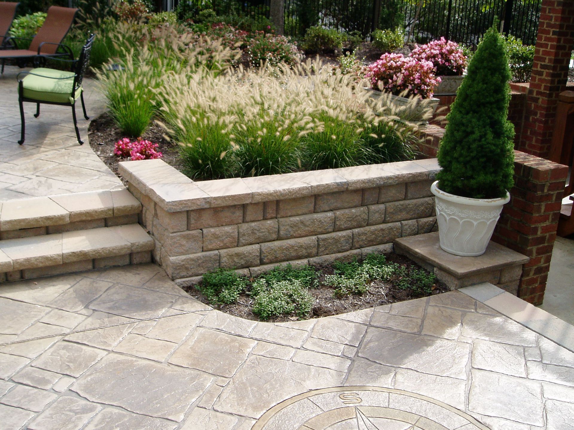Raised garden bed with stone wall, steps, and patio; green and tan hues.