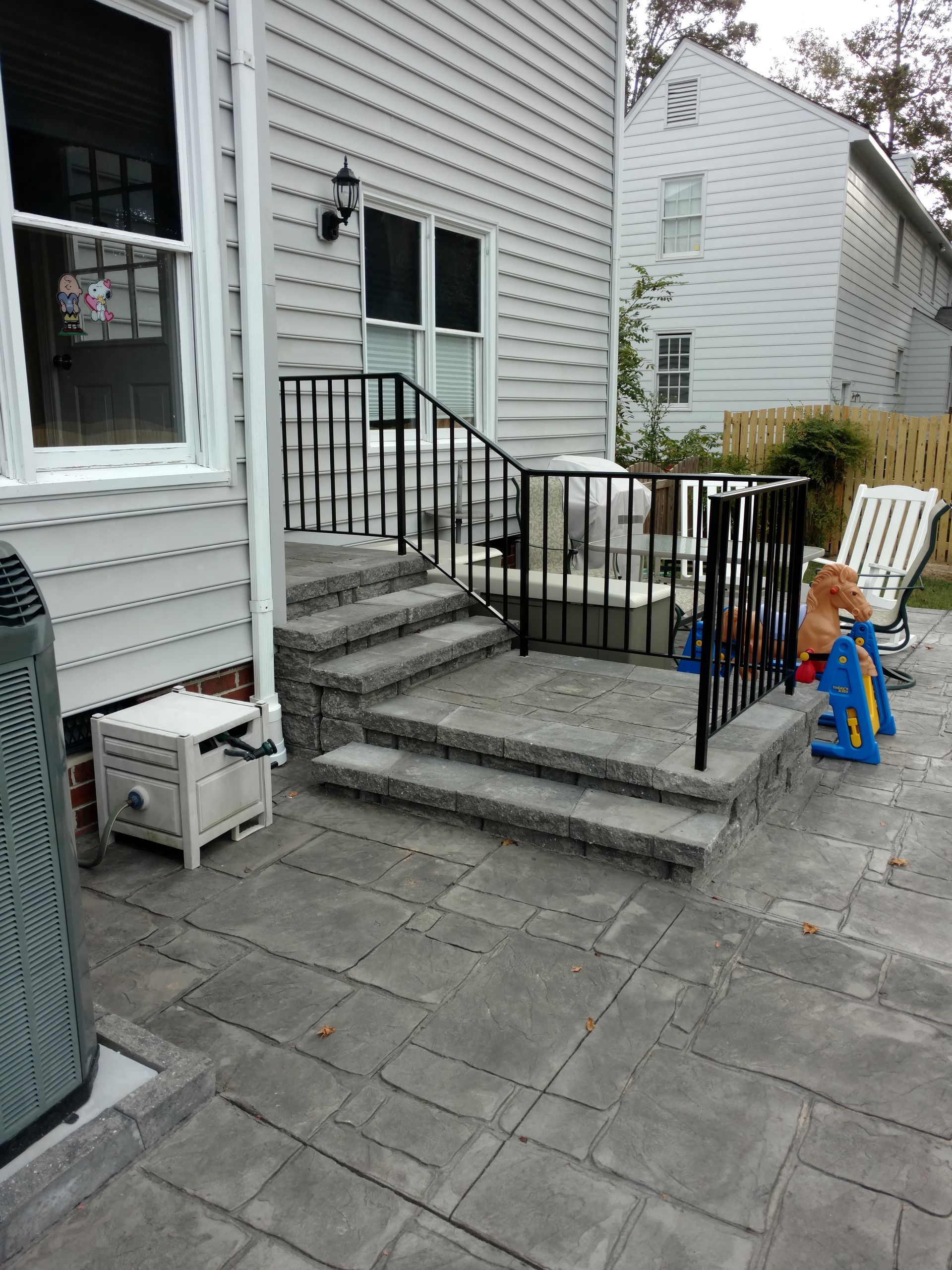 Exterior view of concrete steps with black railing leading to a patio with outdoor furniture.