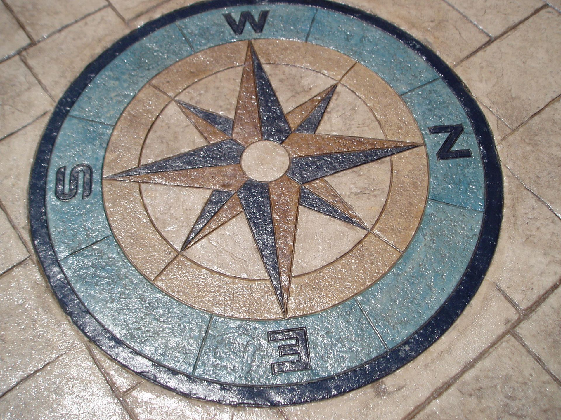 Compass rose design inlaid on a tile floor with blue, tan, and brown colors.