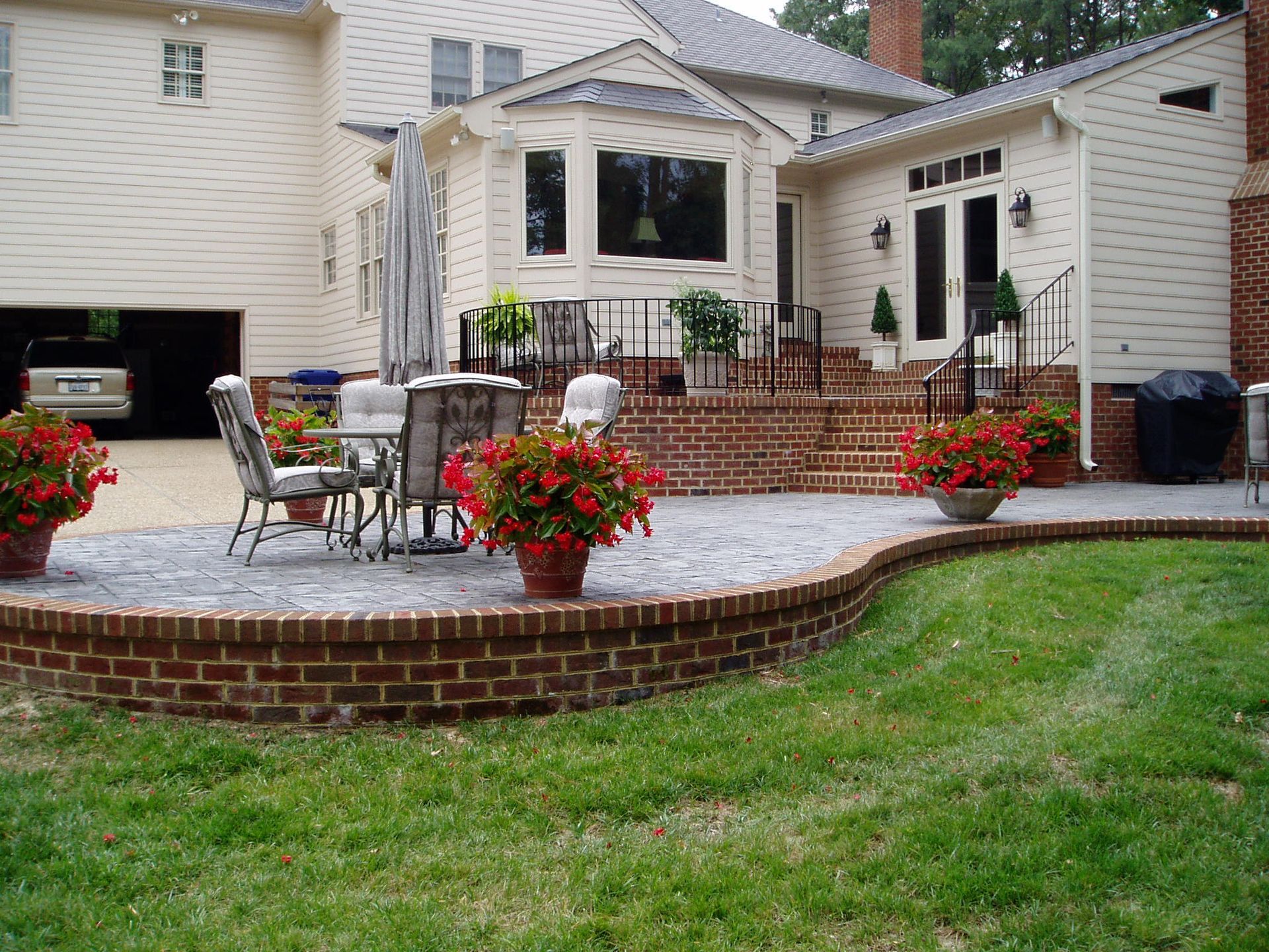 Brick patio with potted red flowers, seating area, and steps leading to a house.