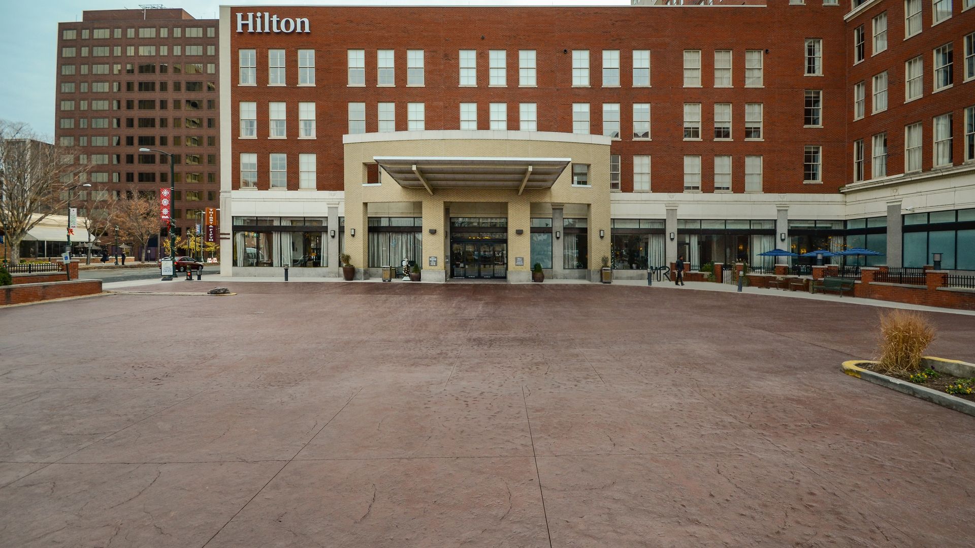 Hilton hotel exterior with brick facade and covered entrance, wide paved area in front.