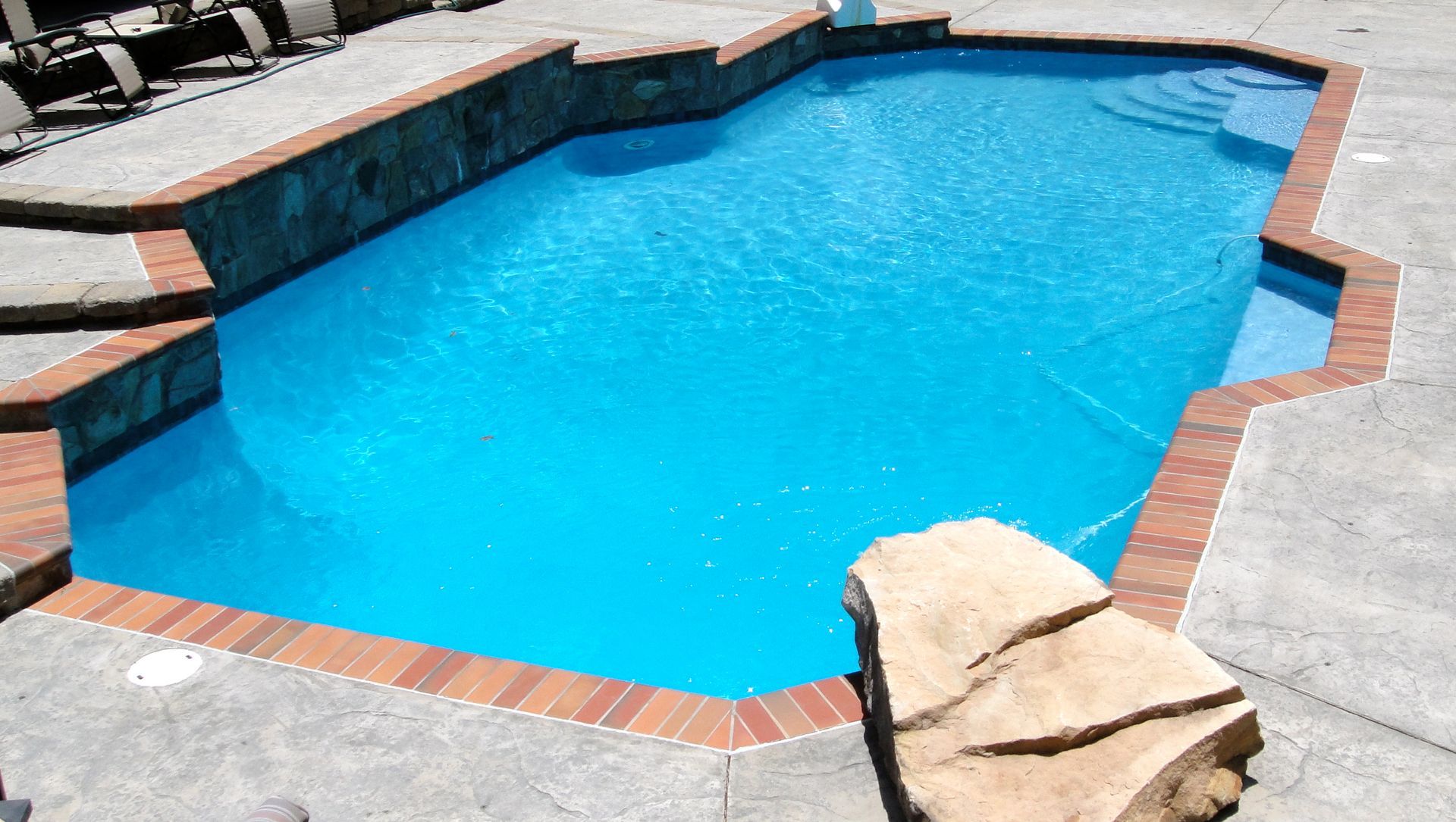 Swimming pool with brick border and rock feature, filled with blue water.