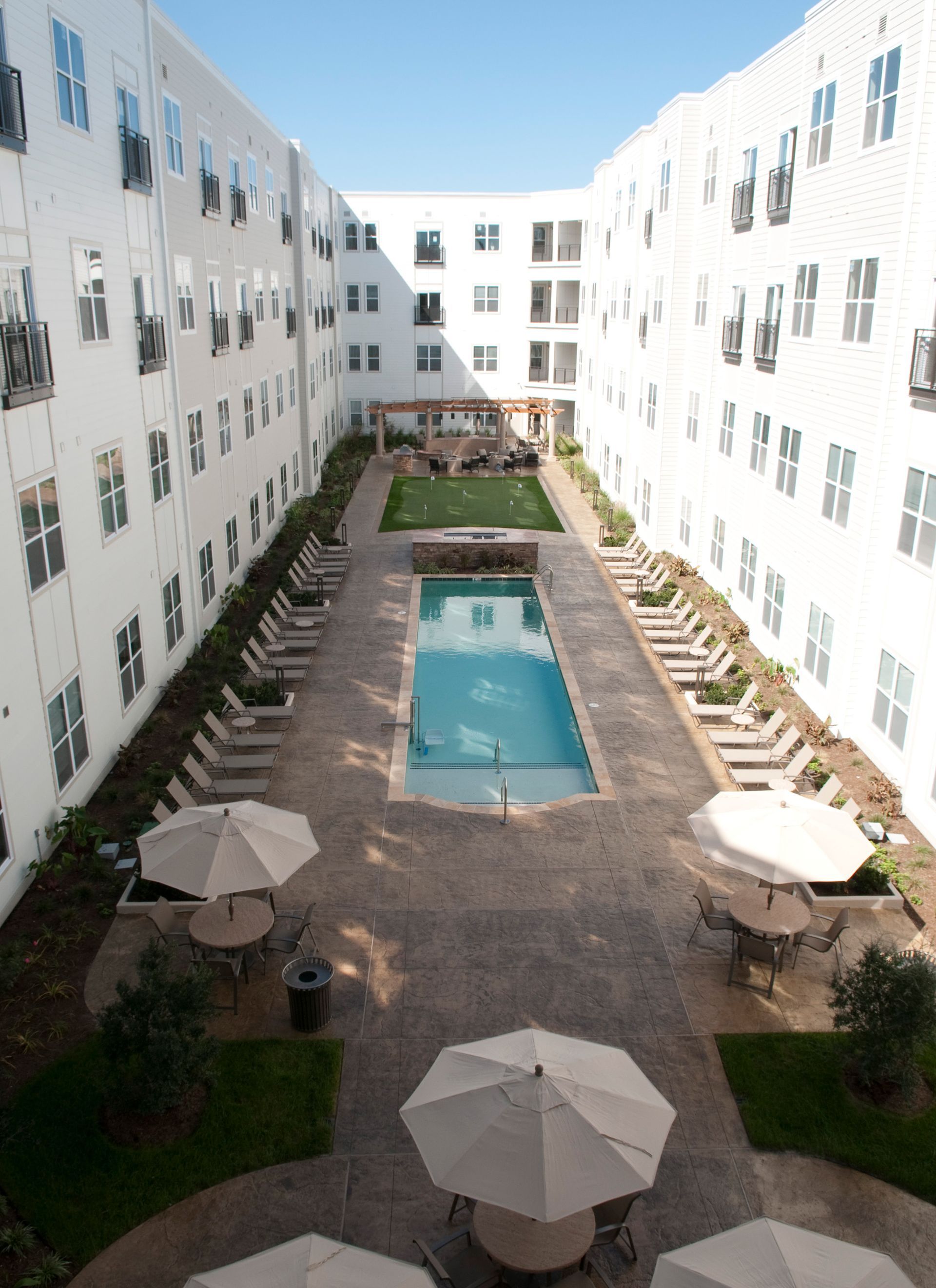 Courtyard with pool, lounge chairs, umbrellas, and white apartment buildings.