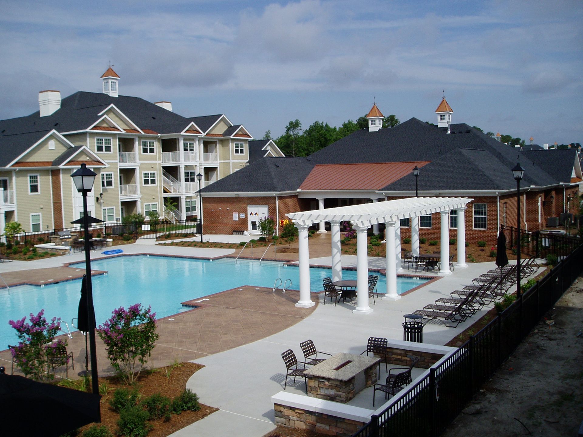 Pool and buildings at an apartment complex under a partly cloudy sky.