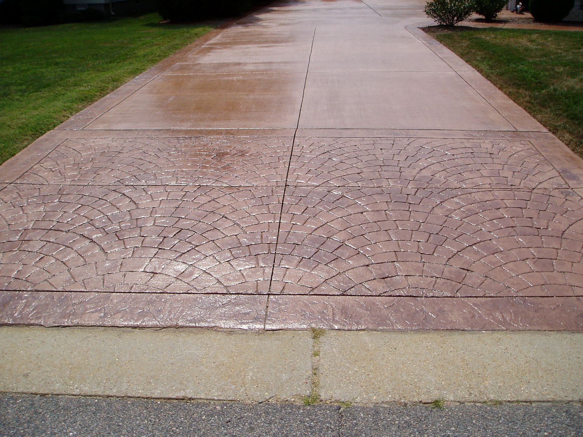 Brown decorative concrete driveway with fan-shaped patterns, surrounded by grass and a beige edge.
