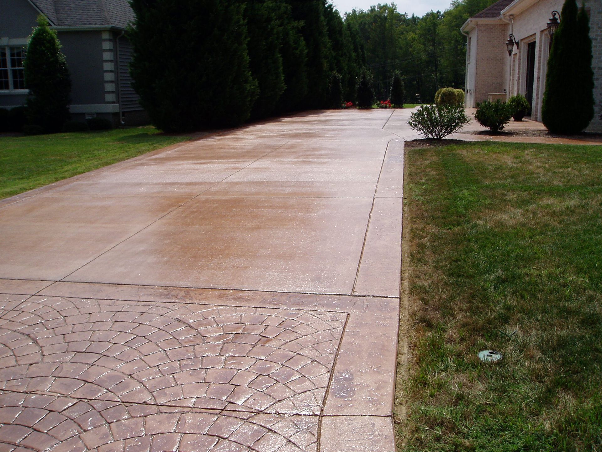 Stamped concrete driveway, brown hue, leading toward a house with green lawn on the side.