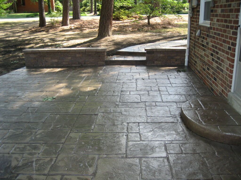 Wet stamped concrete patio next to brick house and low retaining wall.