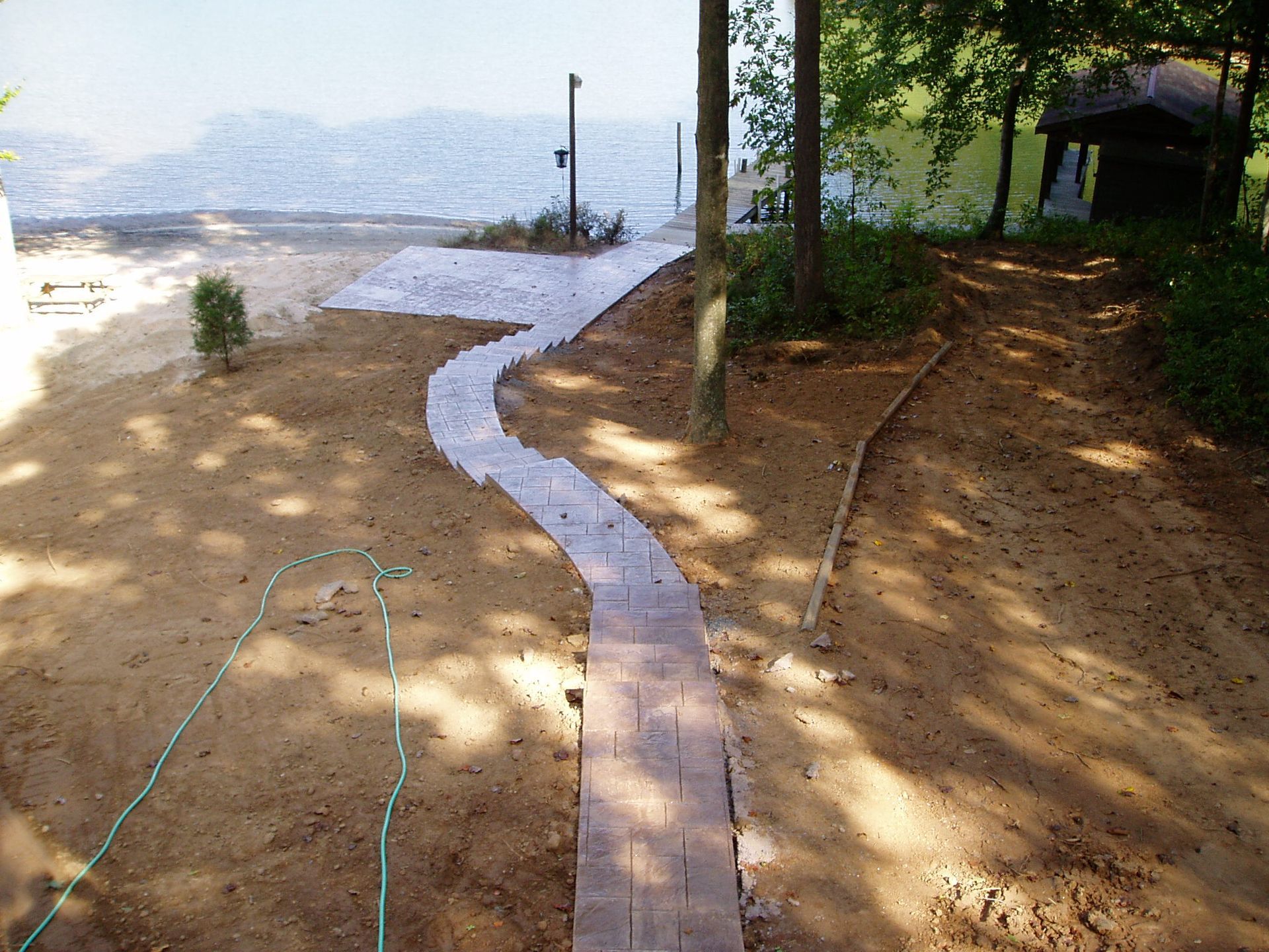 A winding brick pathway leads to a sandy beach. Trees and a small structure border the path.