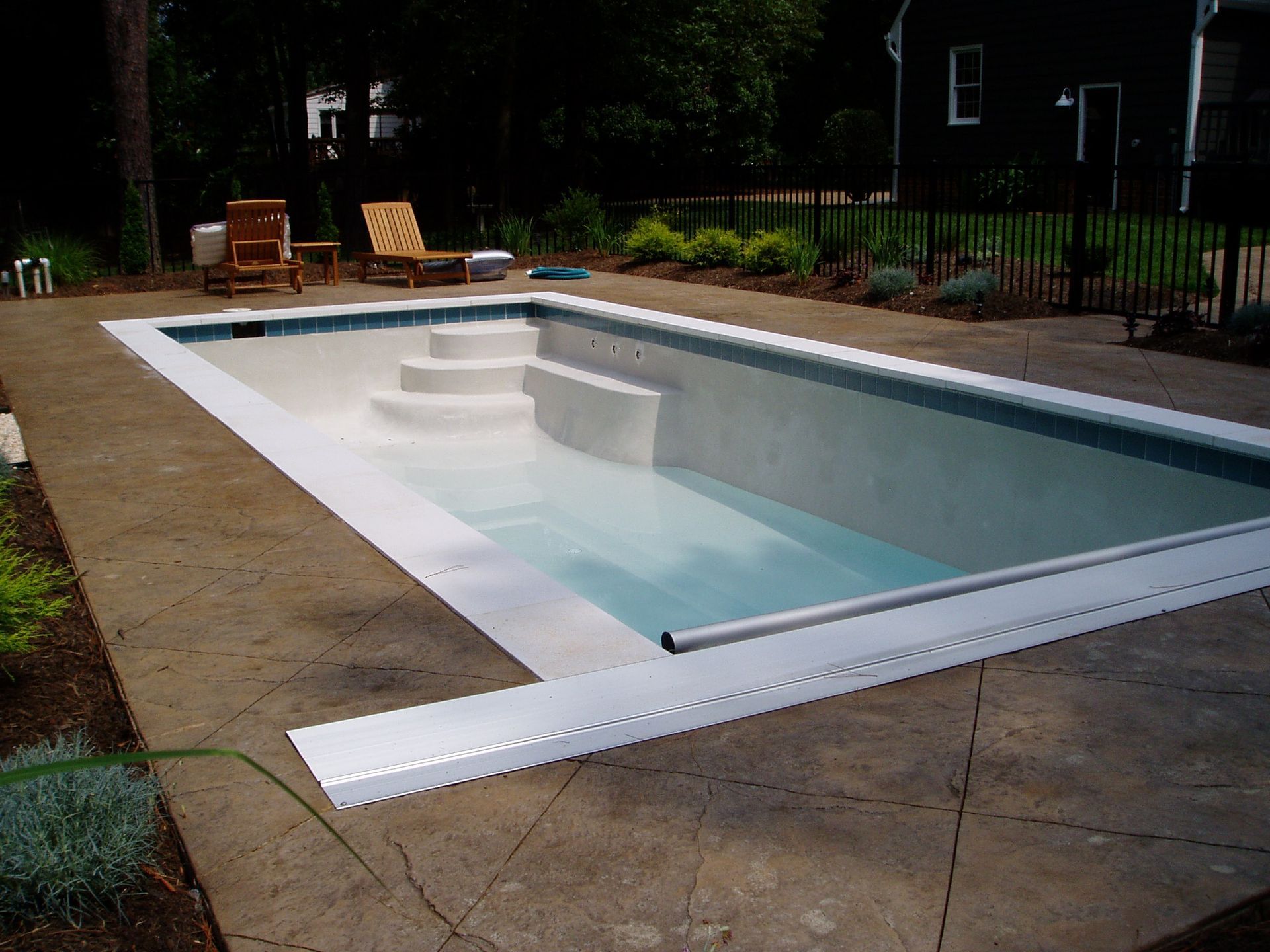 Rectangular in-ground swimming pool with white coping, concrete deck, and steps at one end.