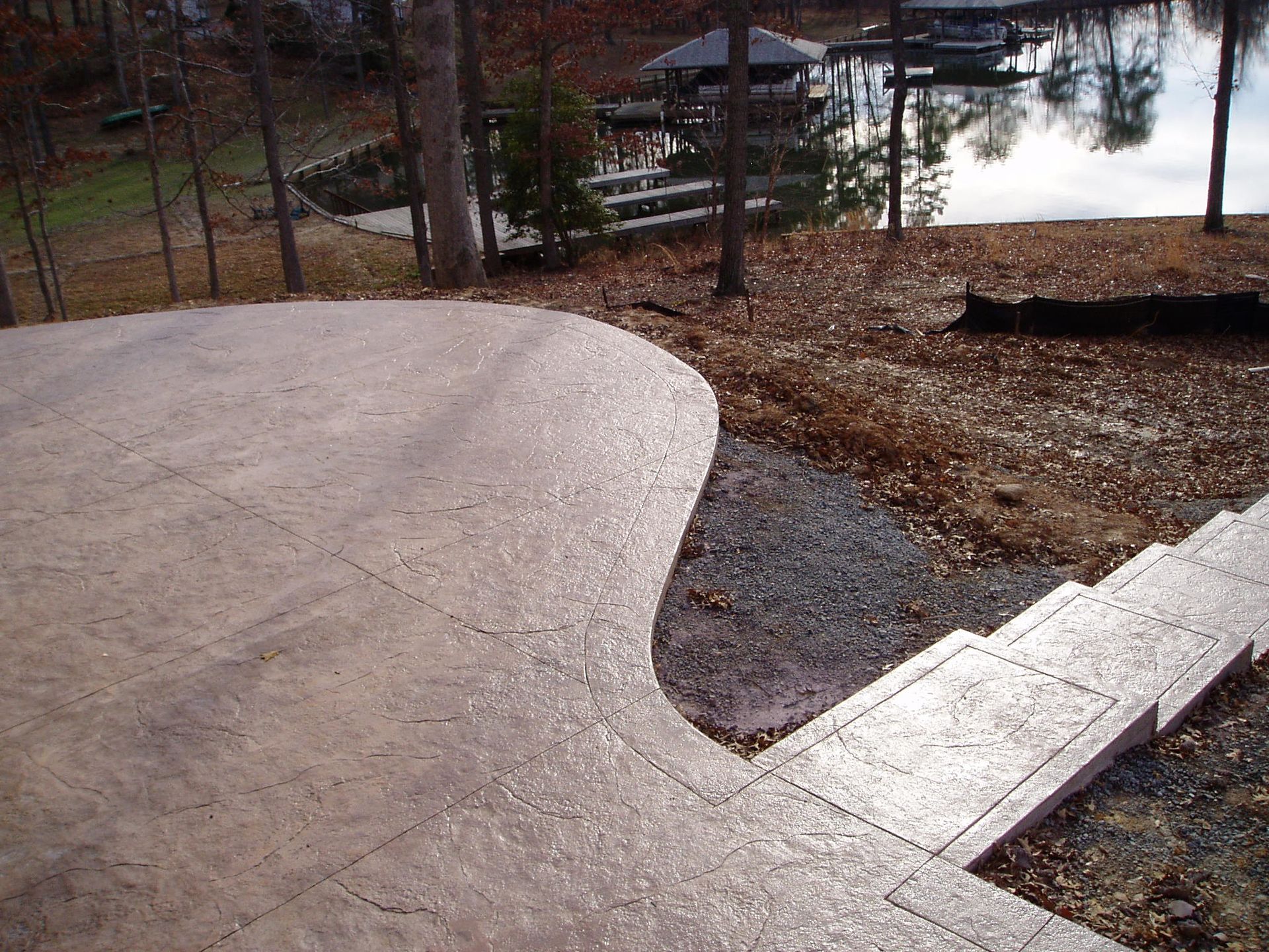 Concrete patio and stairs leading down to a lake, surrounded by trees and fallen leaves.