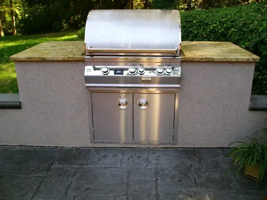 Stainless steel outdoor grill built into a stone structure with countertop.