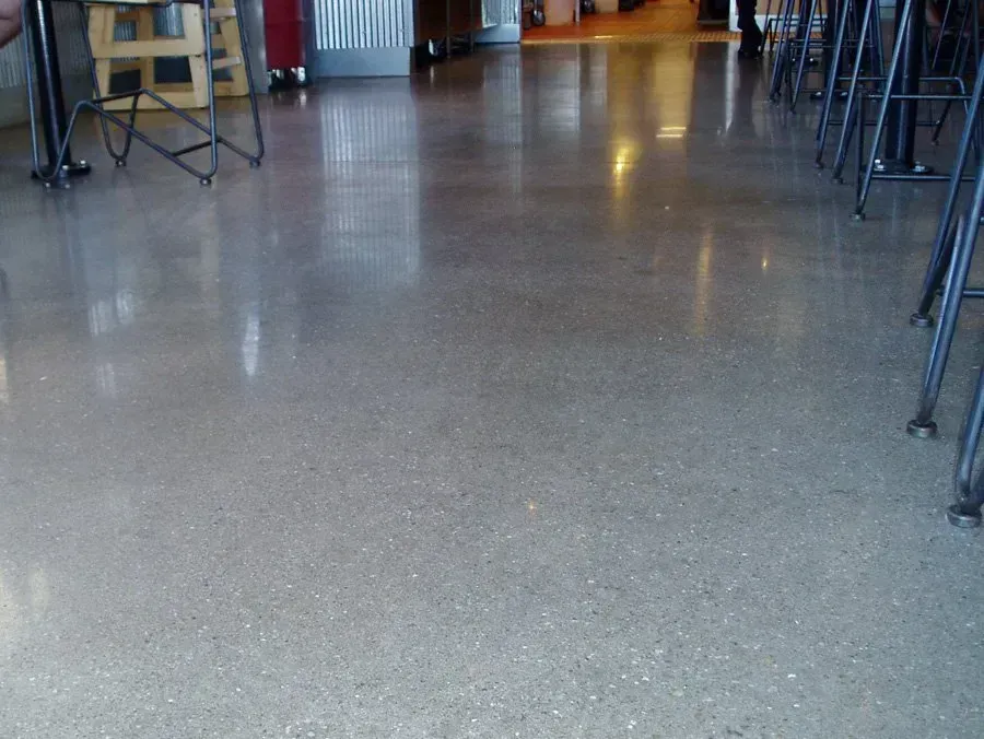 Polished concrete floor in a commercial space, reflecting ambient light. Tables and chairs are in the background.