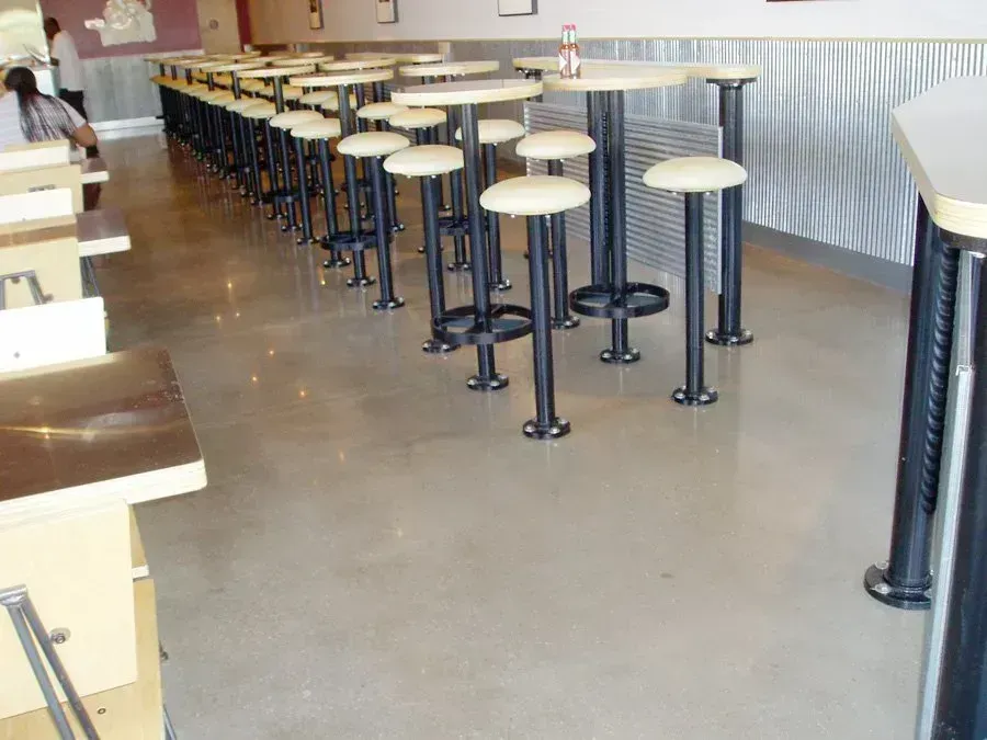 Restaurant interior with polished concrete floor, tables, stools, and wall with corrugated metal.