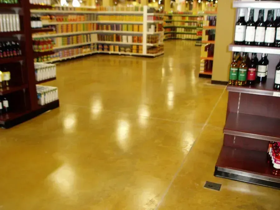 Polished, yellow-toned concrete floor in a brightly lit grocery store aisle with product-filled shelves.