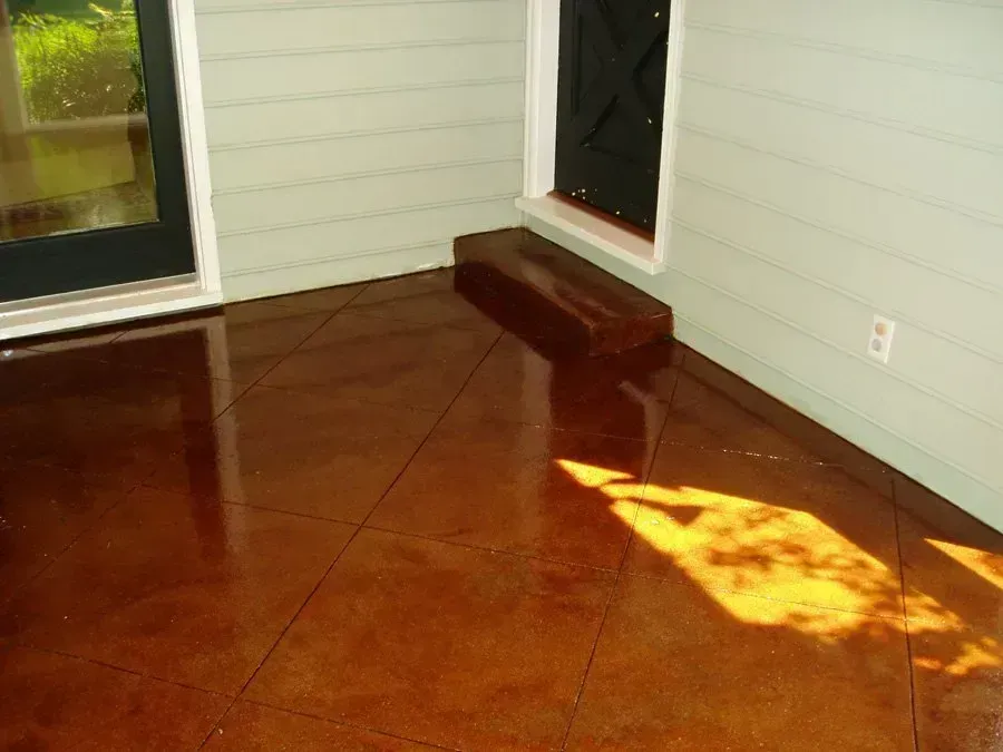 Glossy brown-stained concrete floor with dark lines; a small step, black door, and green-painted walls.