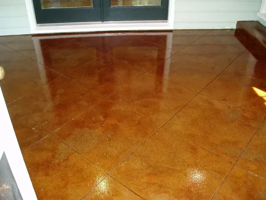 Brown, stained concrete patio with grid pattern. Double doors in the background reflect light.