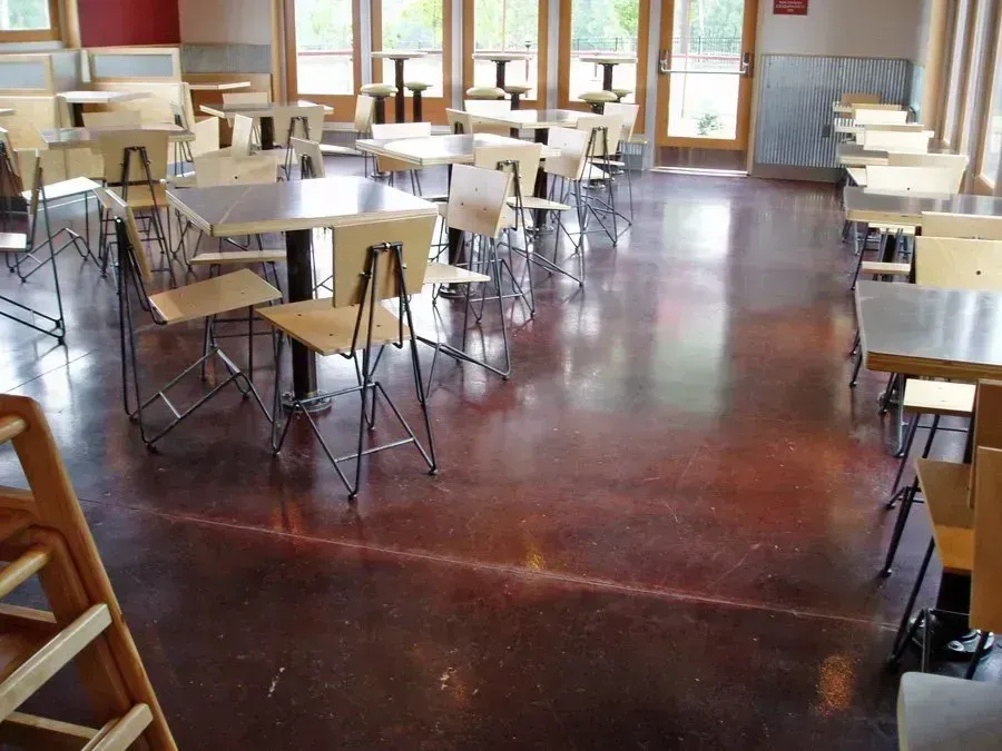 Cafe interior with square tables, chairs, and stained concrete floor.