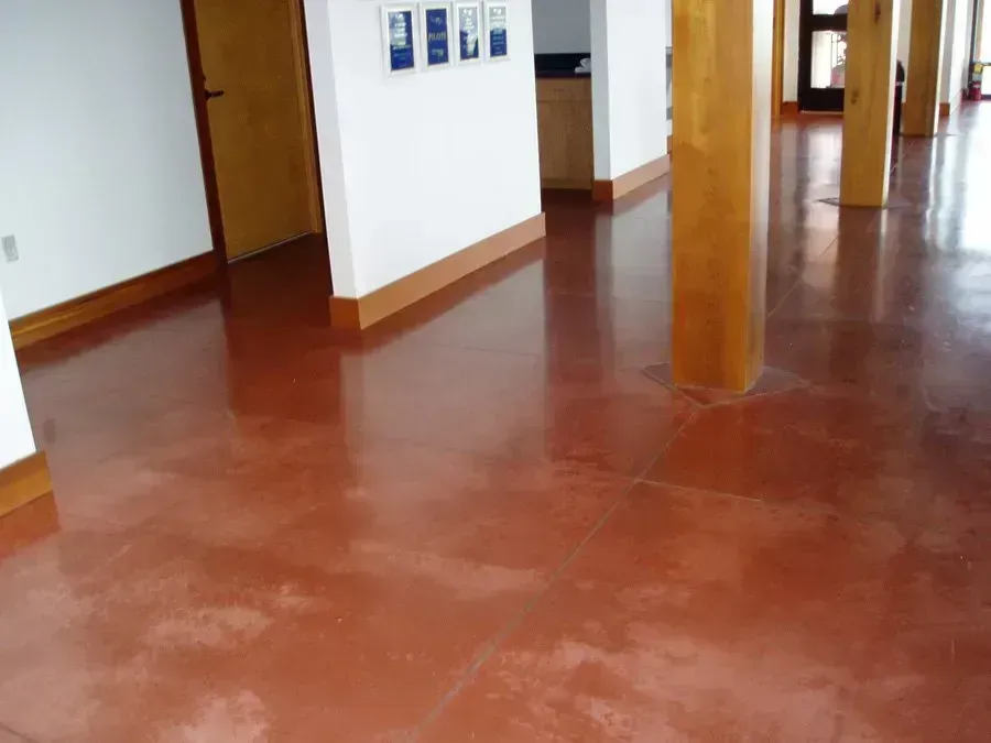 Red polished concrete floor in a building, with wood trim, columns, and a doorway.