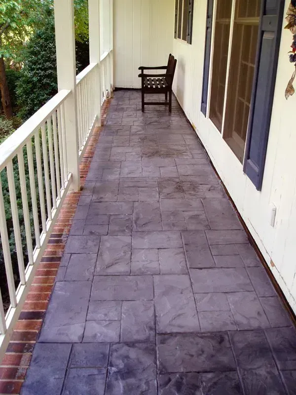 A porch with a patterned gray floor, white railing, and a dark wooden chair.